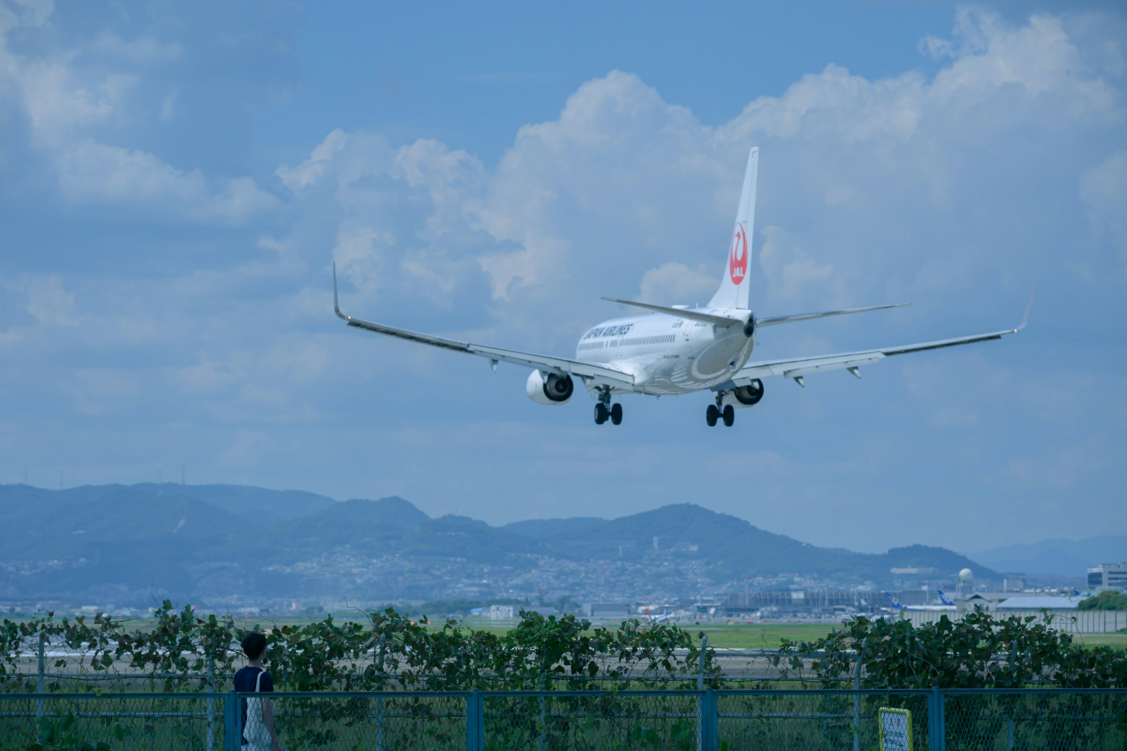 Flugzeug landet vor blauem Himmel mit Wolken und umliegender Landschaft