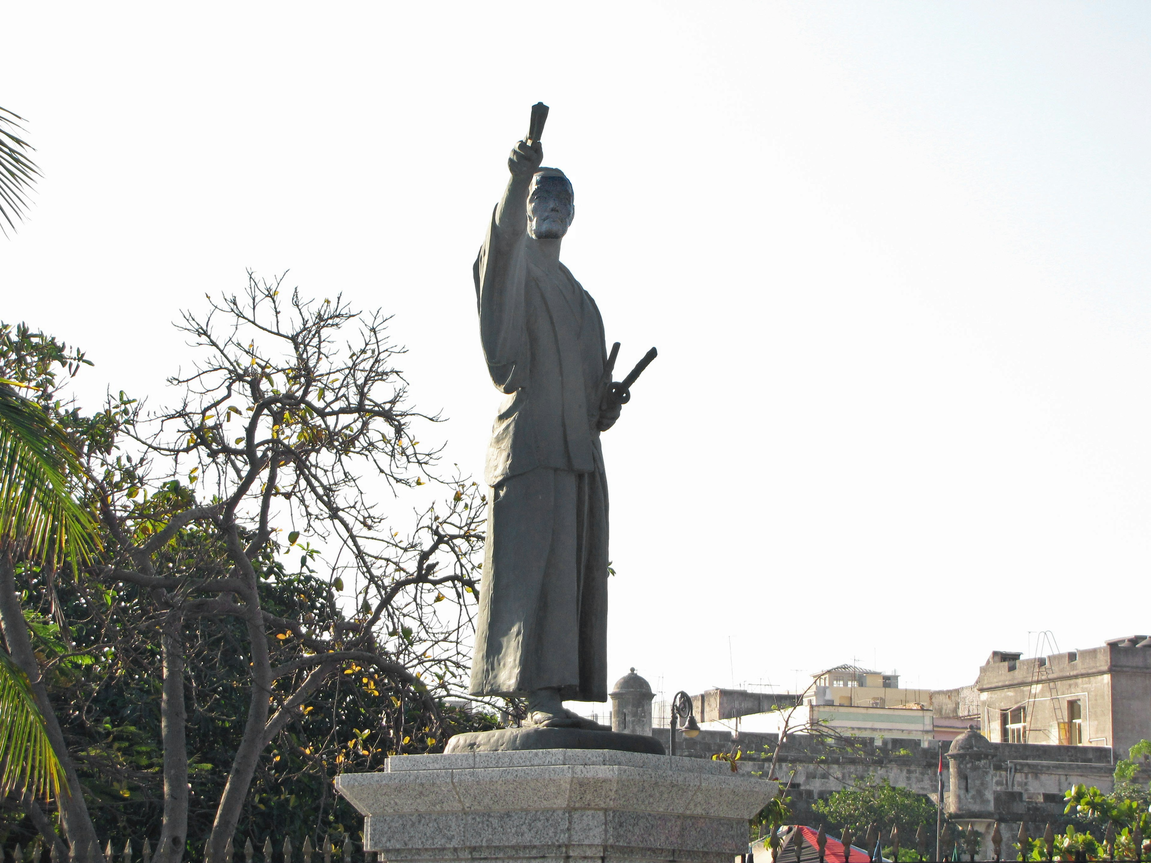 Una estatua de bronce de un guerrero de pie sobre un alto pedestal contra un cielo azul