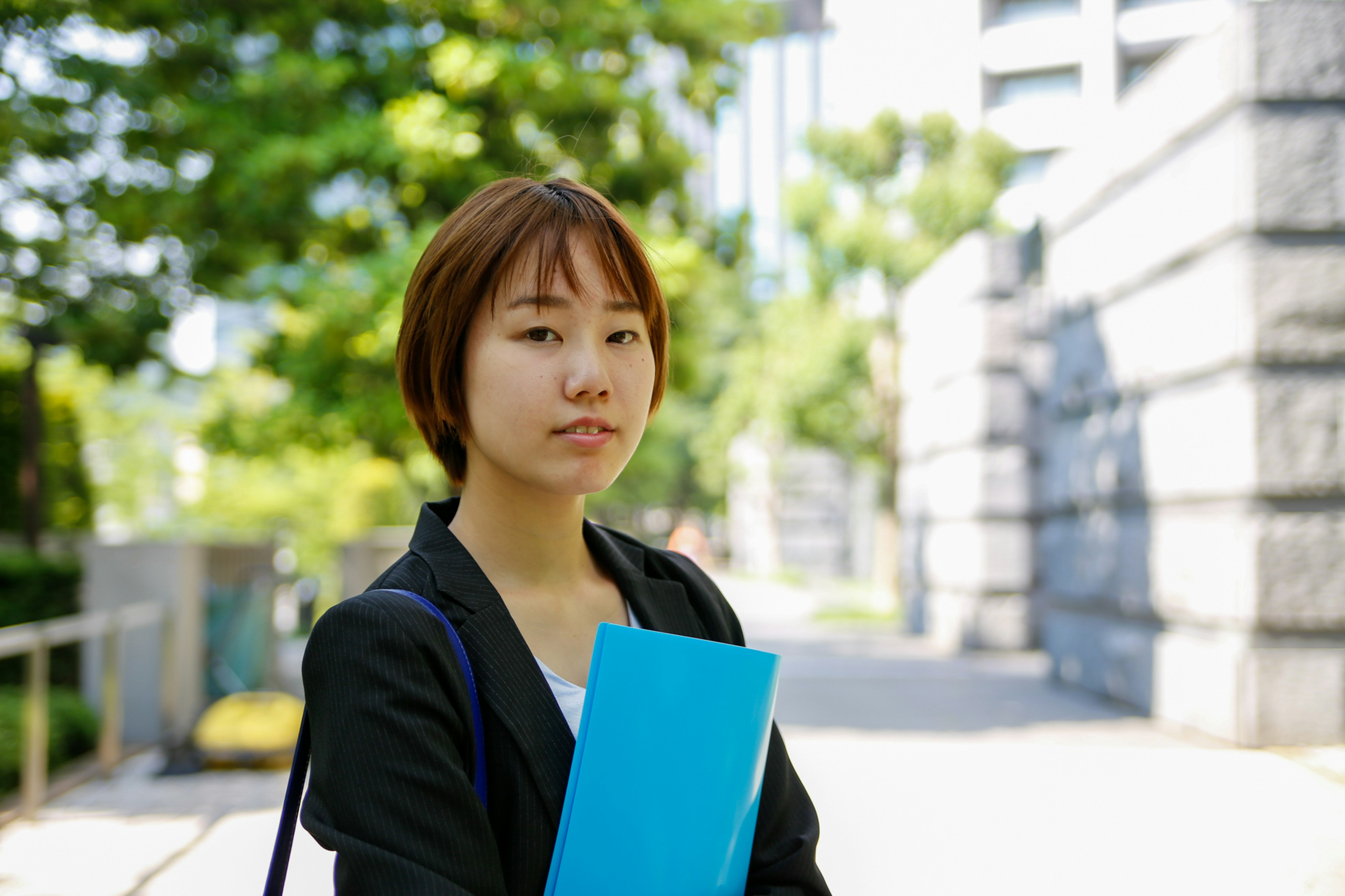 A woman in a business suit holding a blue folder standing in an outdoor urban setting