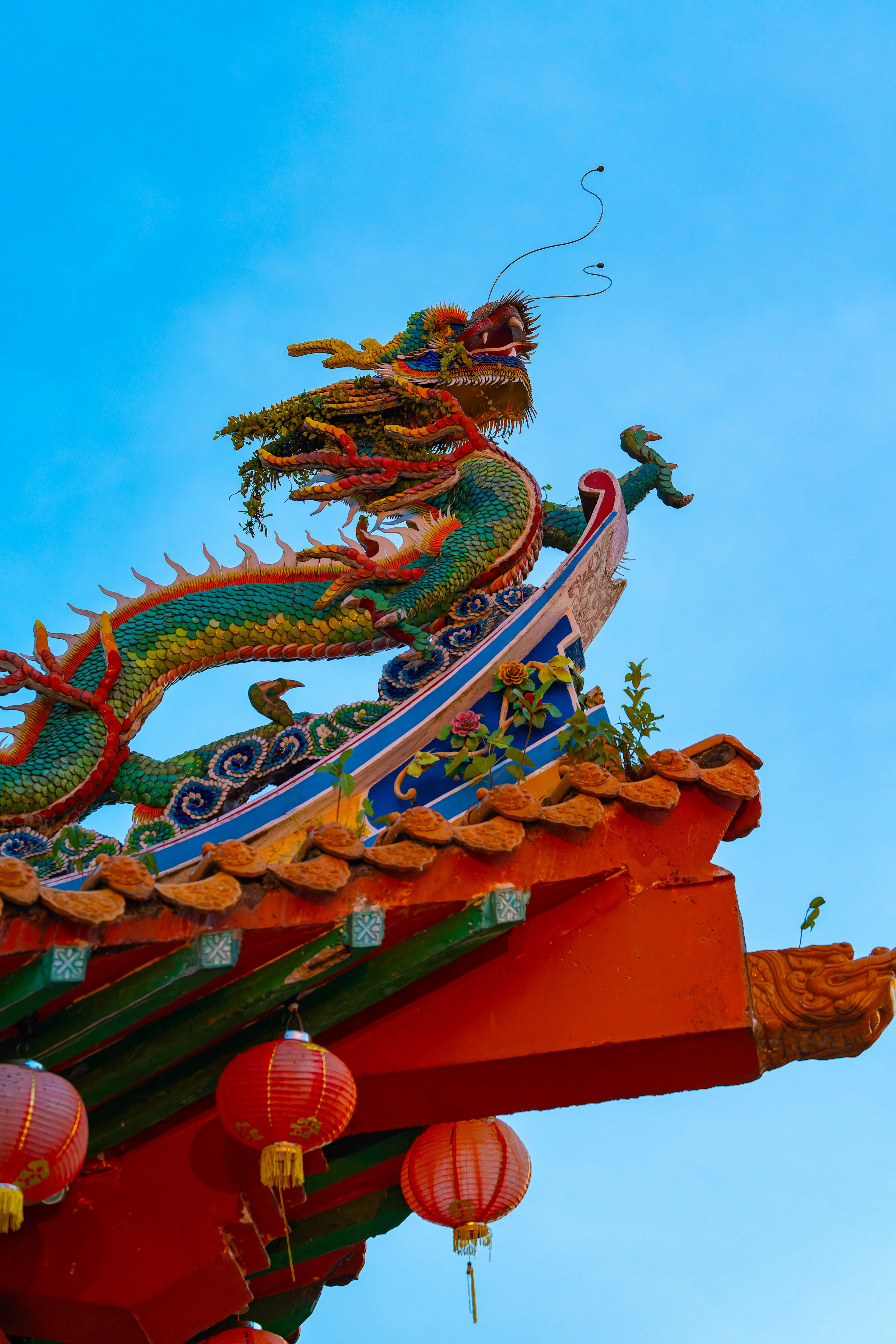 Escultura de dragón colorida y faroles en un techo bajo un cielo azul