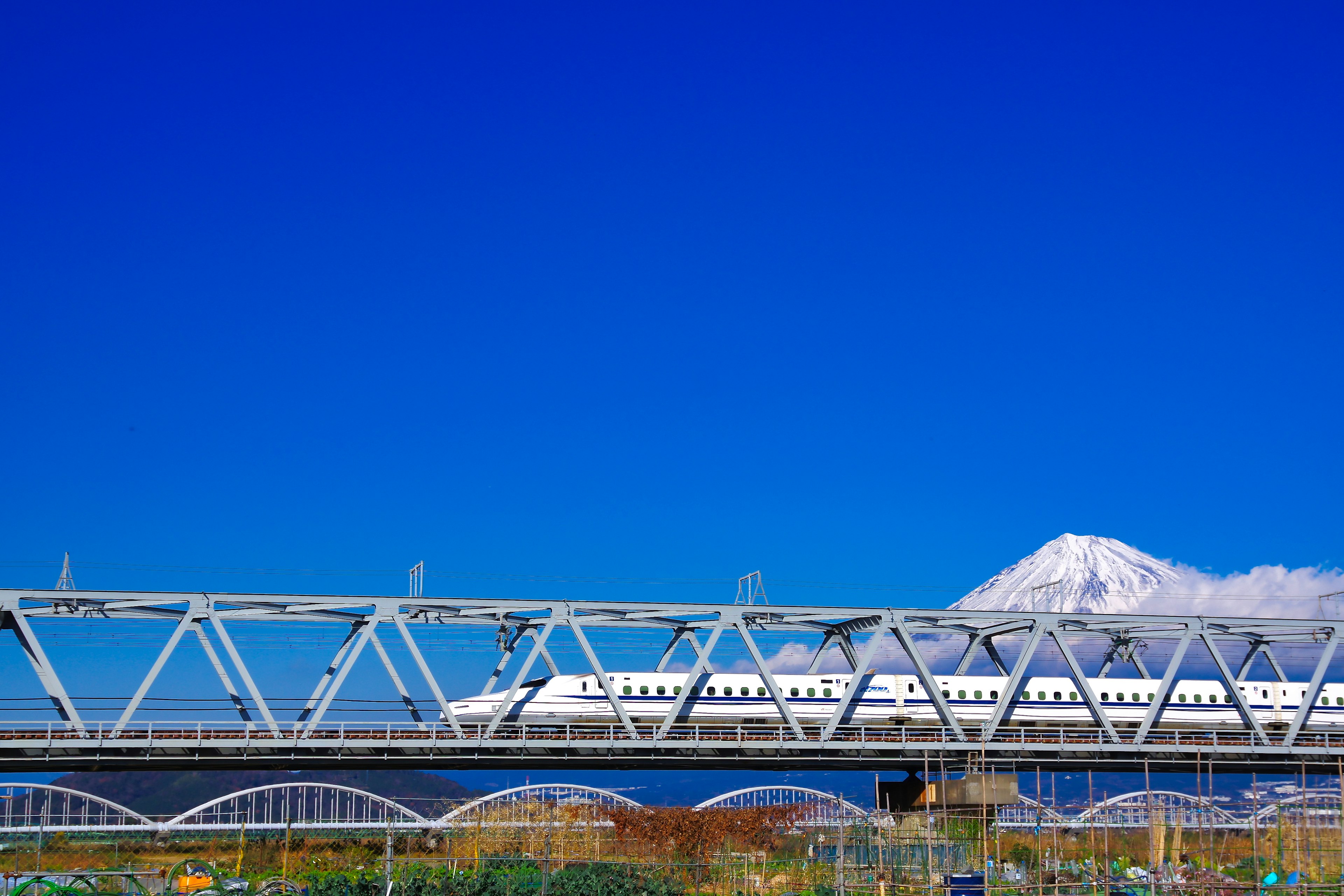 A scenic view featuring Mount Fuji and a Shinkansen bridge under a blue sky