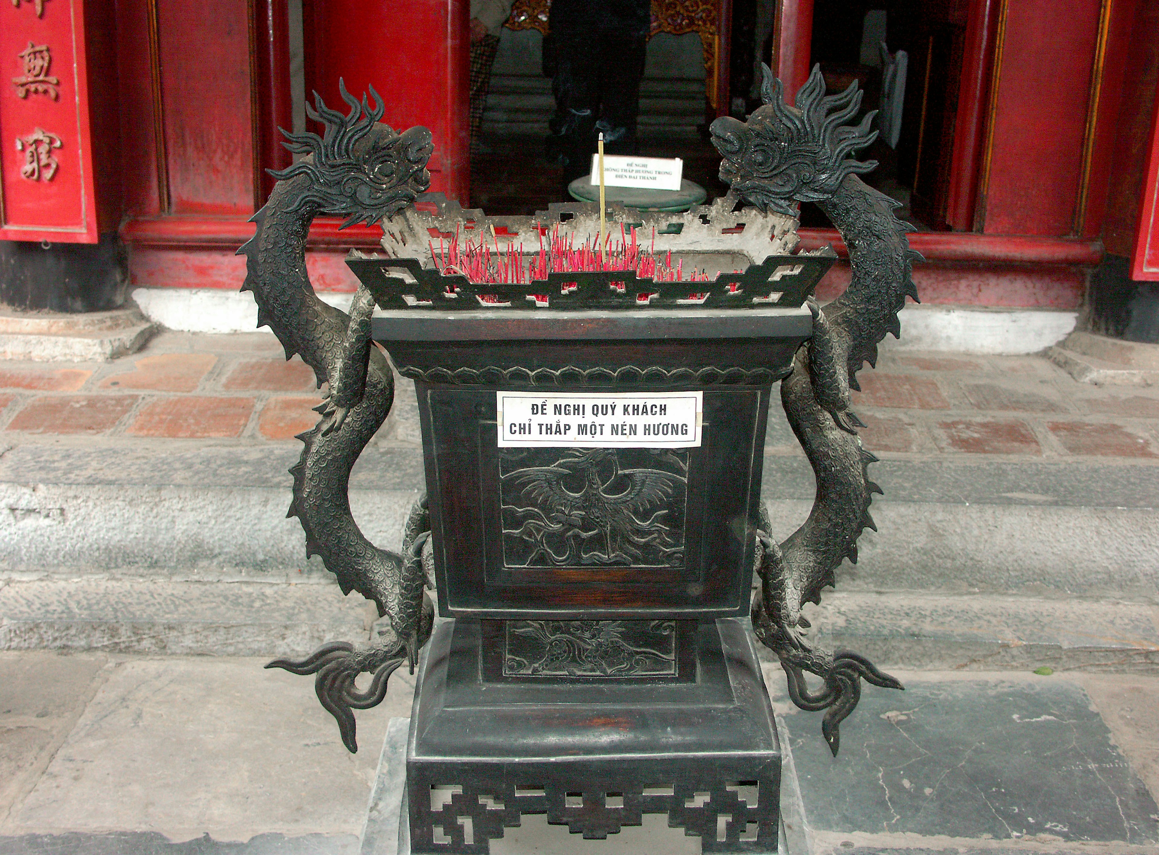 Brûleur d'encens en métal noir avec deux sculptures de dragon et un petit drapeau blanc devant