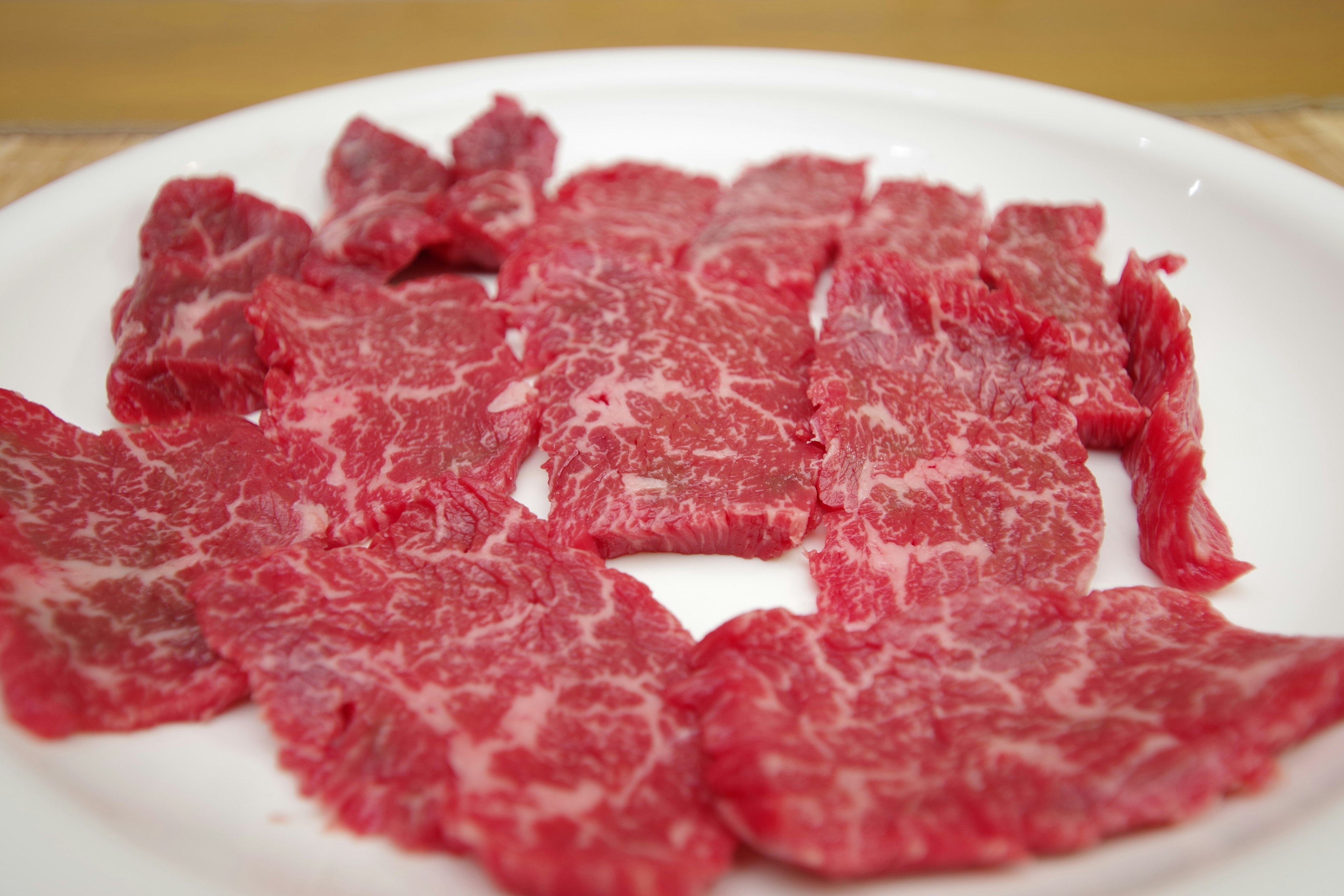 Fette di manzo Wagyu affettate sottili disposte su un piatto bianco