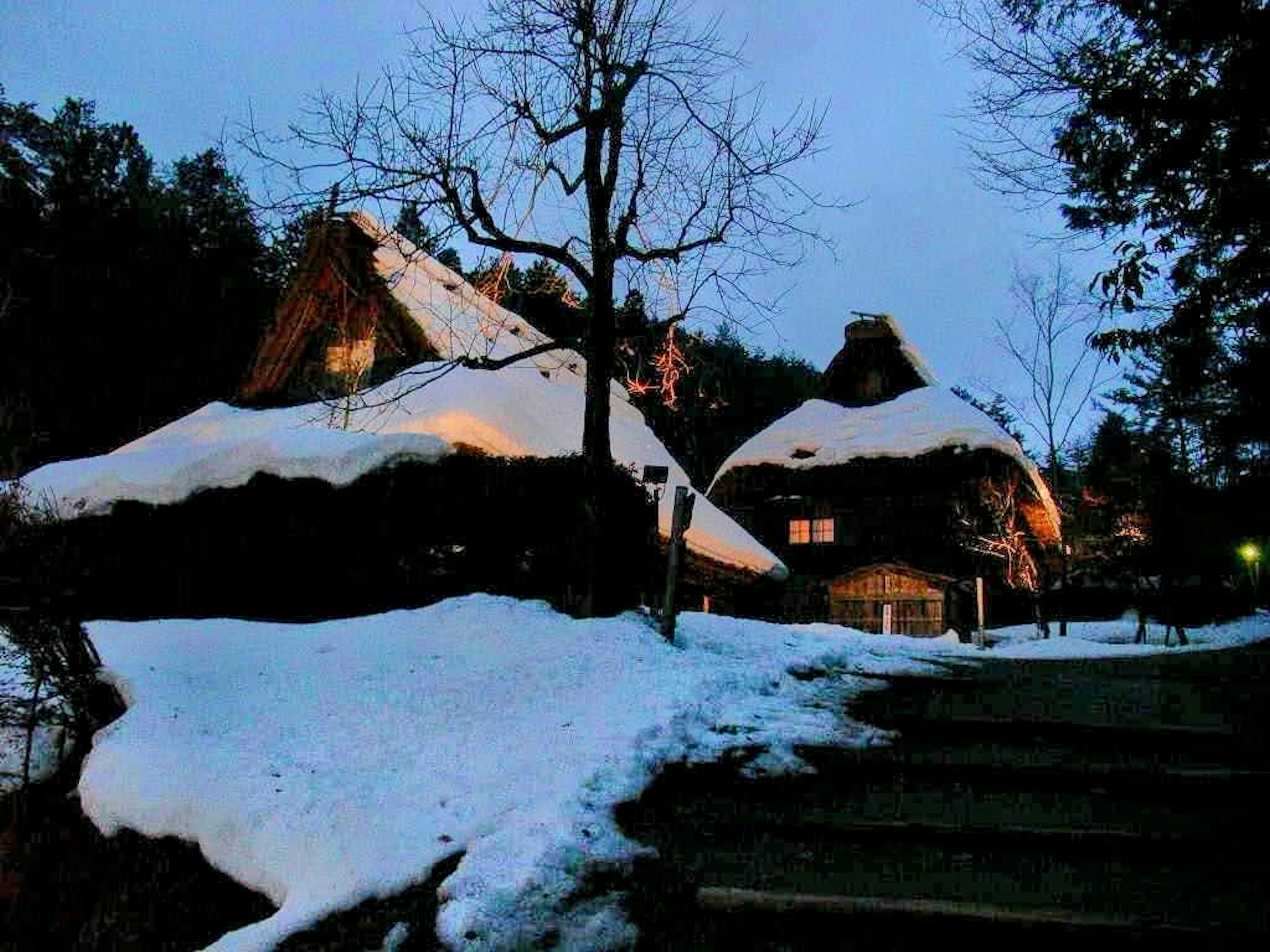 Maisons japonaises traditionnelles recouvertes de neige sous une lumière du soir tamisée