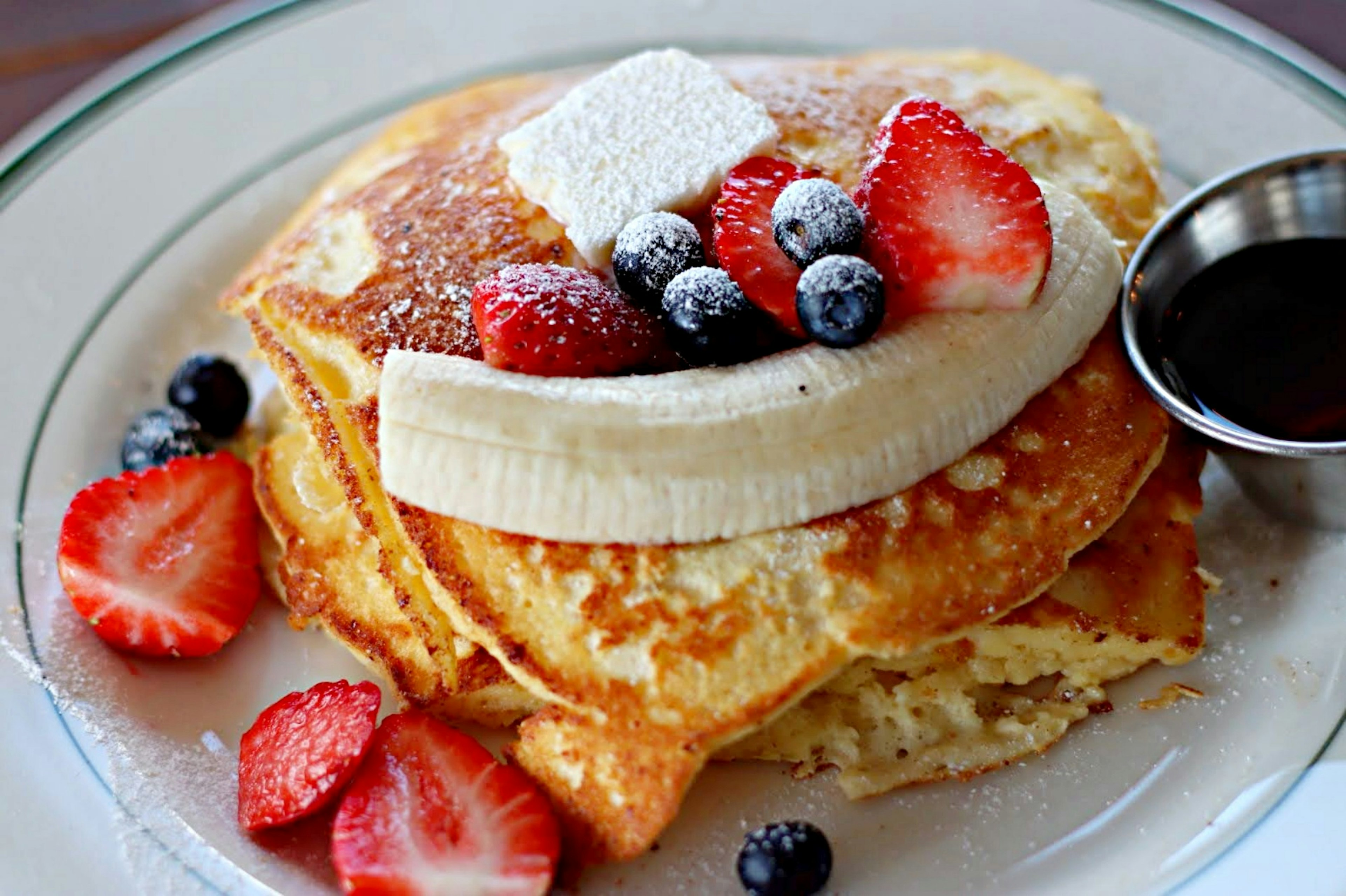 Fluffy pancakes topped with banana, strawberries, and blueberries served with syrup