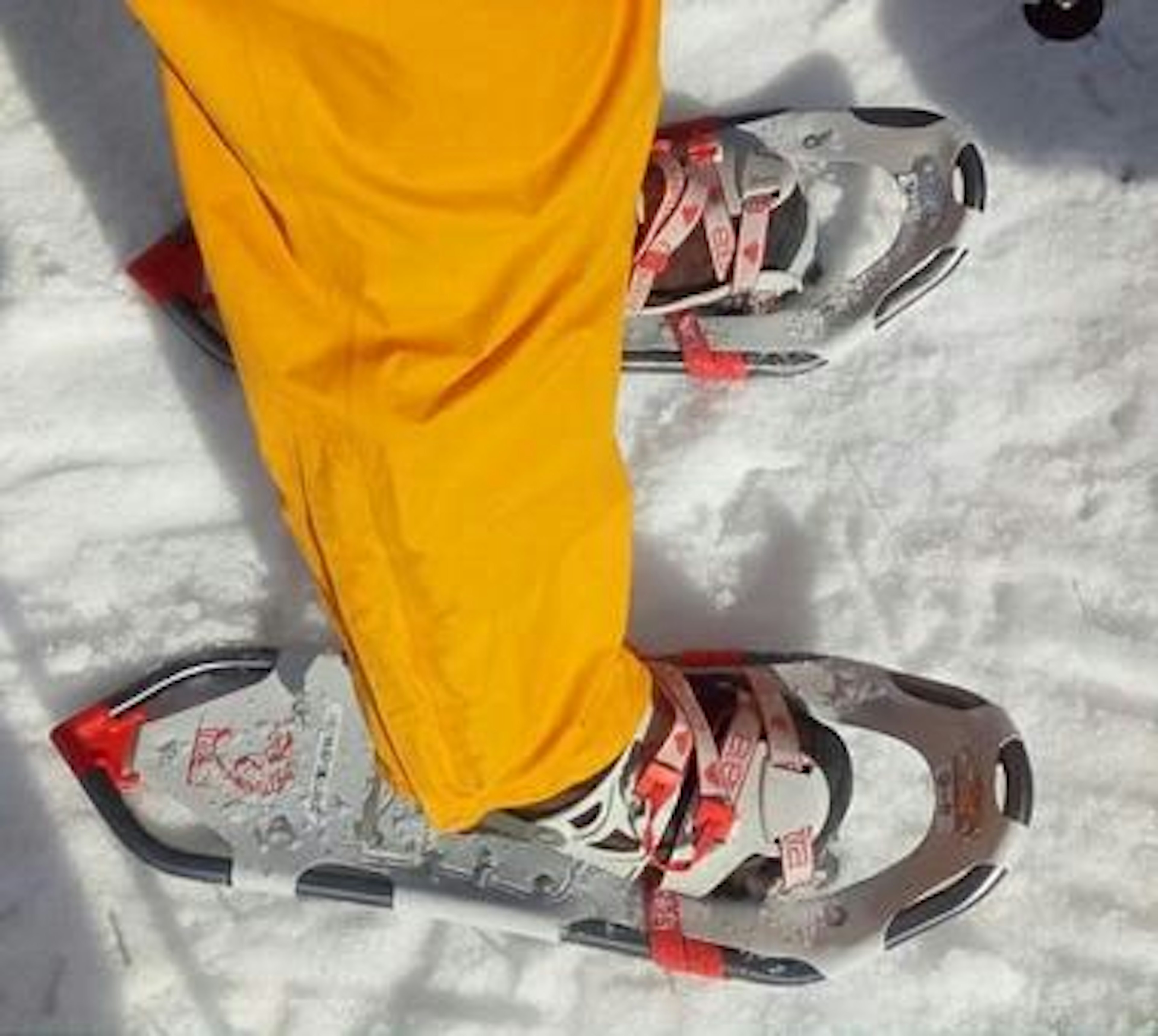 Foot in yellow pants standing on snow with snowshoe attached