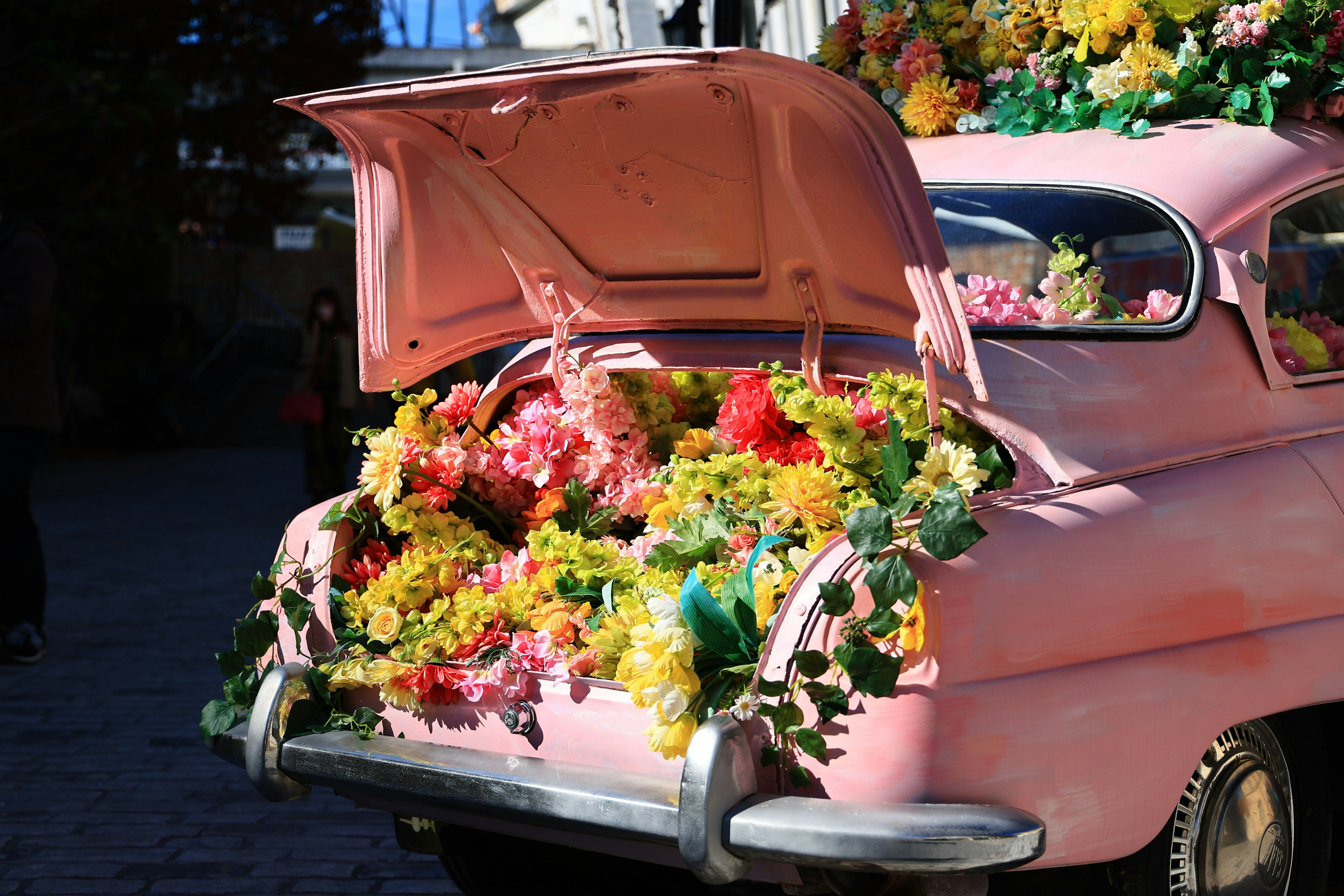 ピンクの車のトランクに色とりどりの花がいっぱい詰まっている