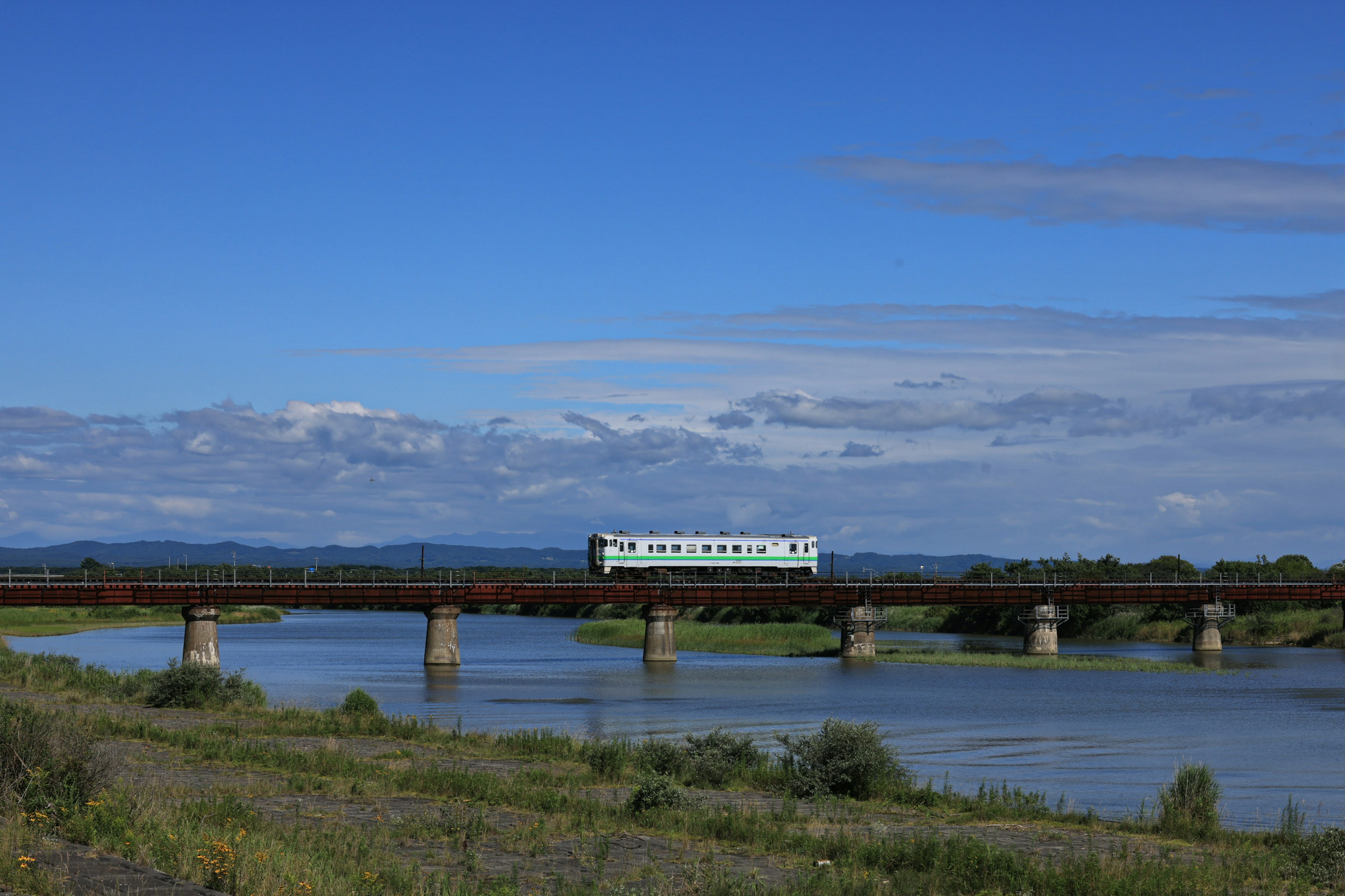 Scène d'un train vert traversant une rivière sous un ciel bleu