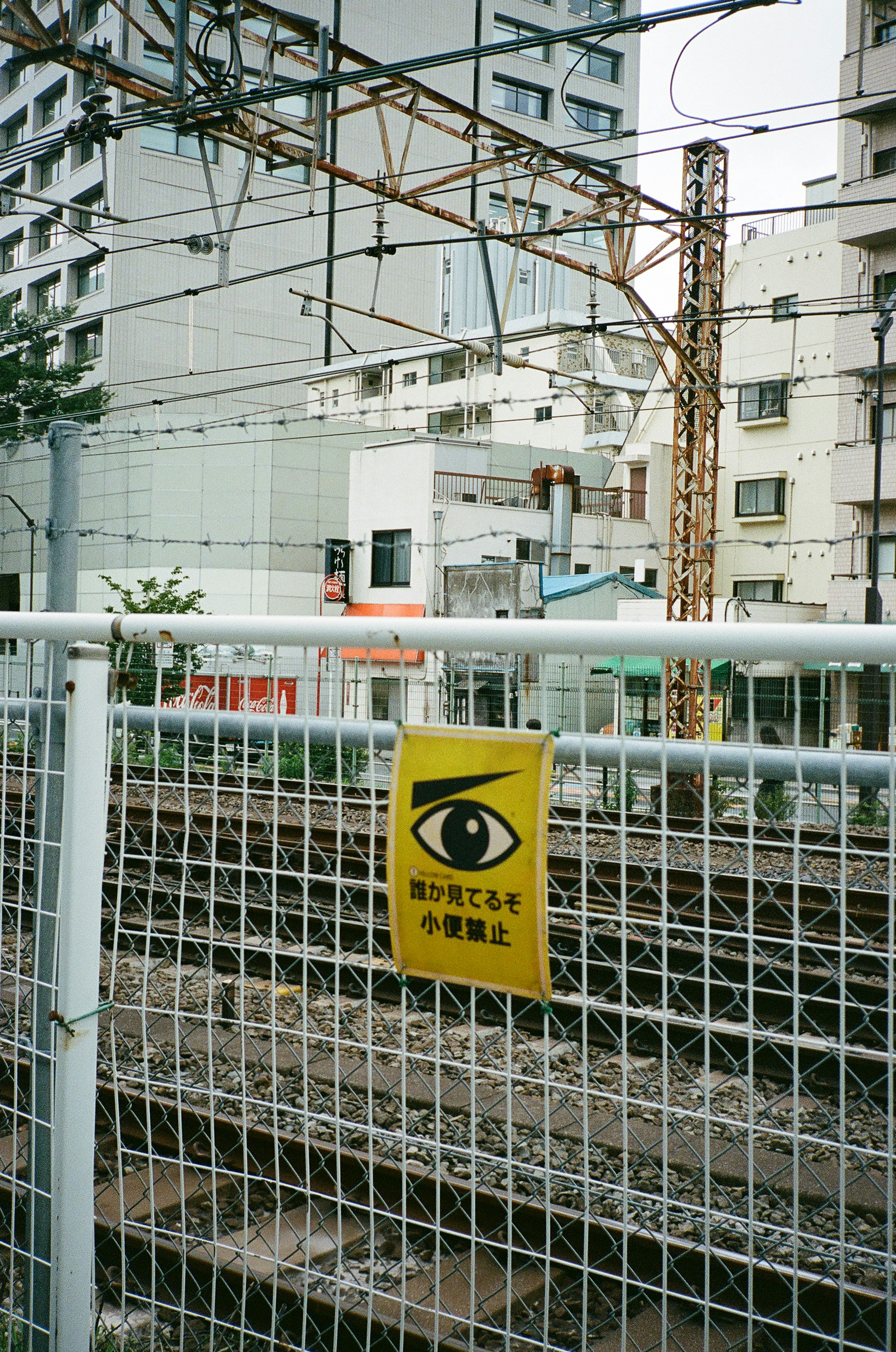 鉄道の線路の前にある目のマークの警告サインと周囲の建物