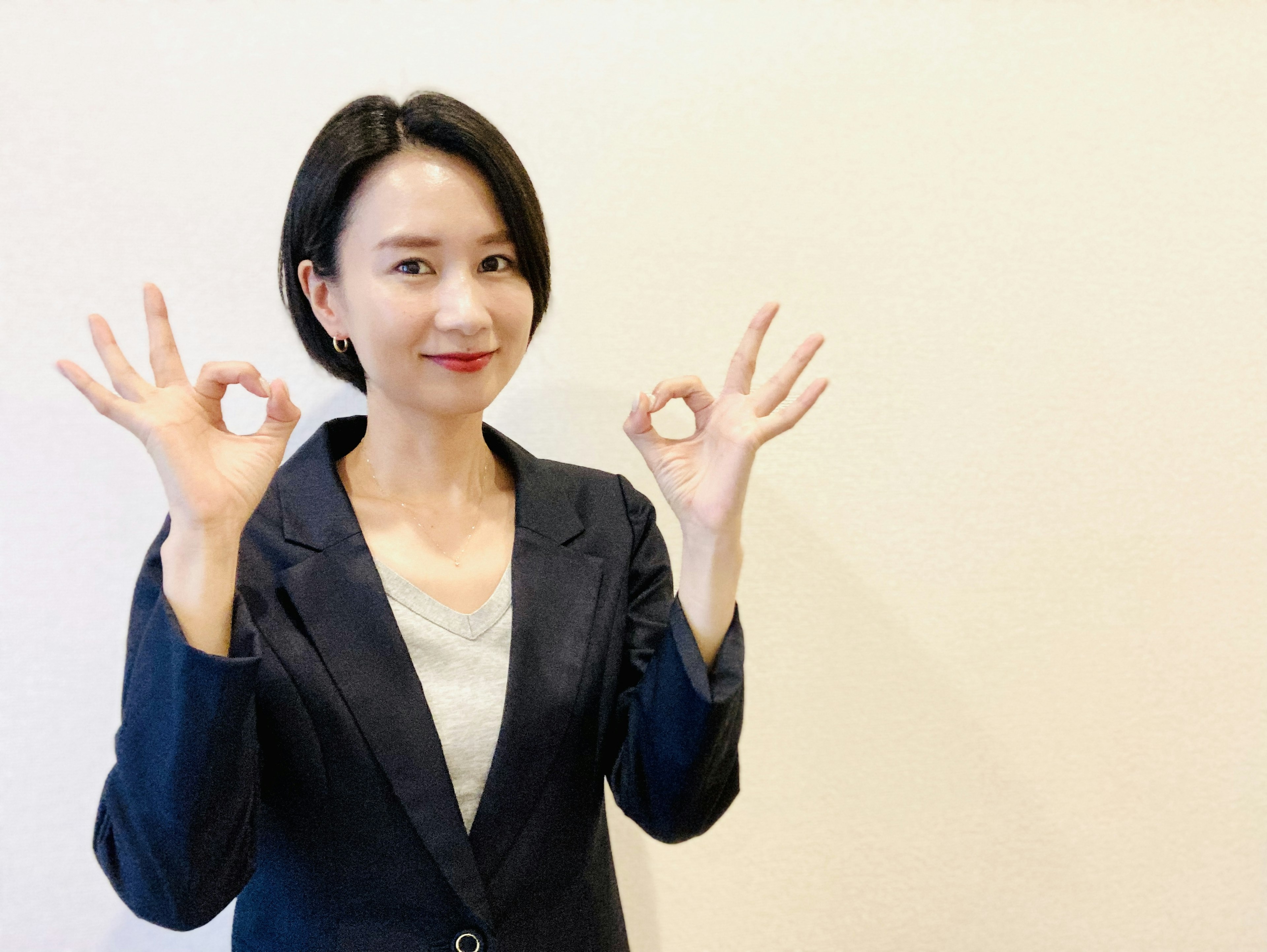 A woman in a suit making OK signs with both hands