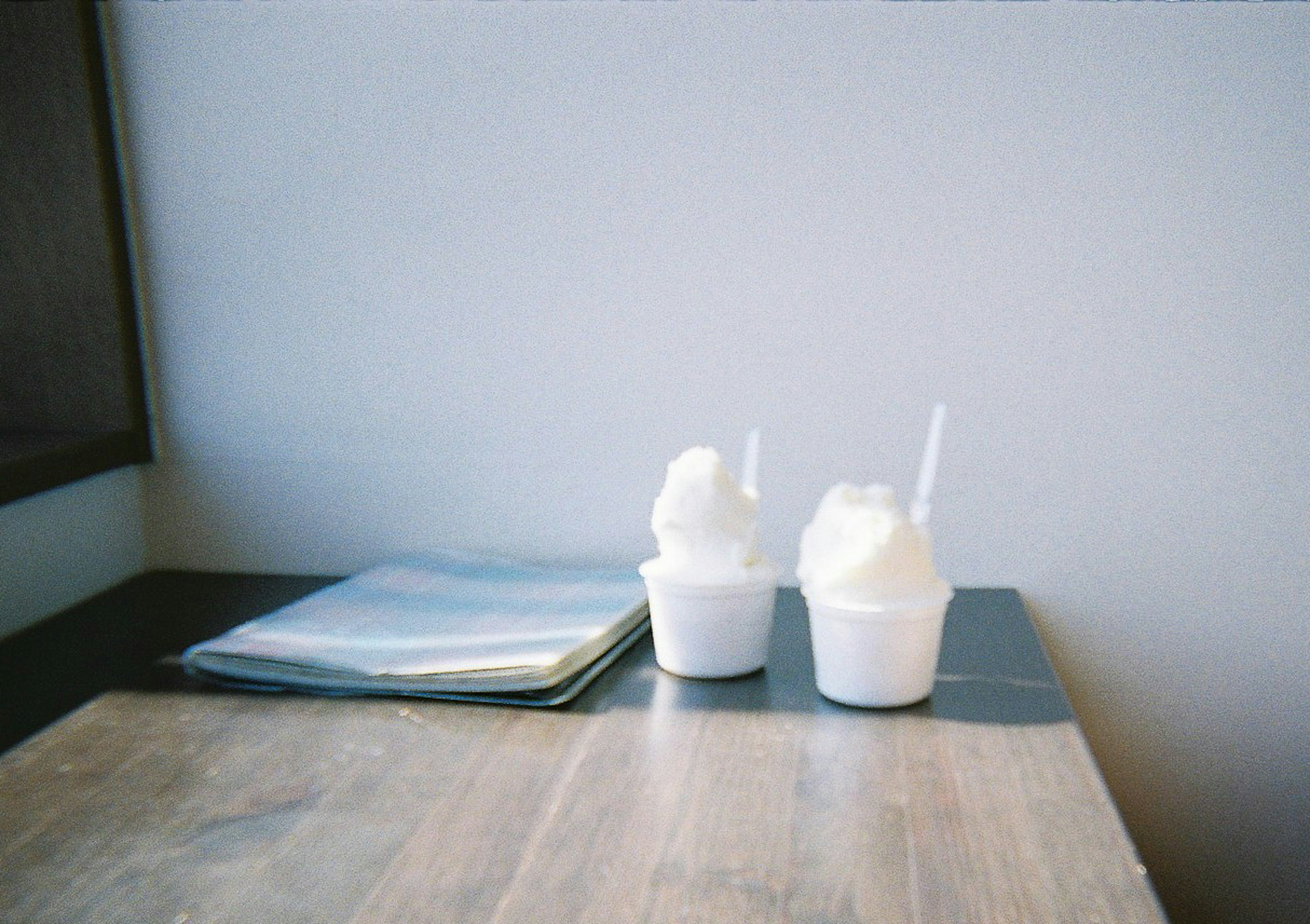 Two white drink containers with straws on a wooden table next to a blue magazine