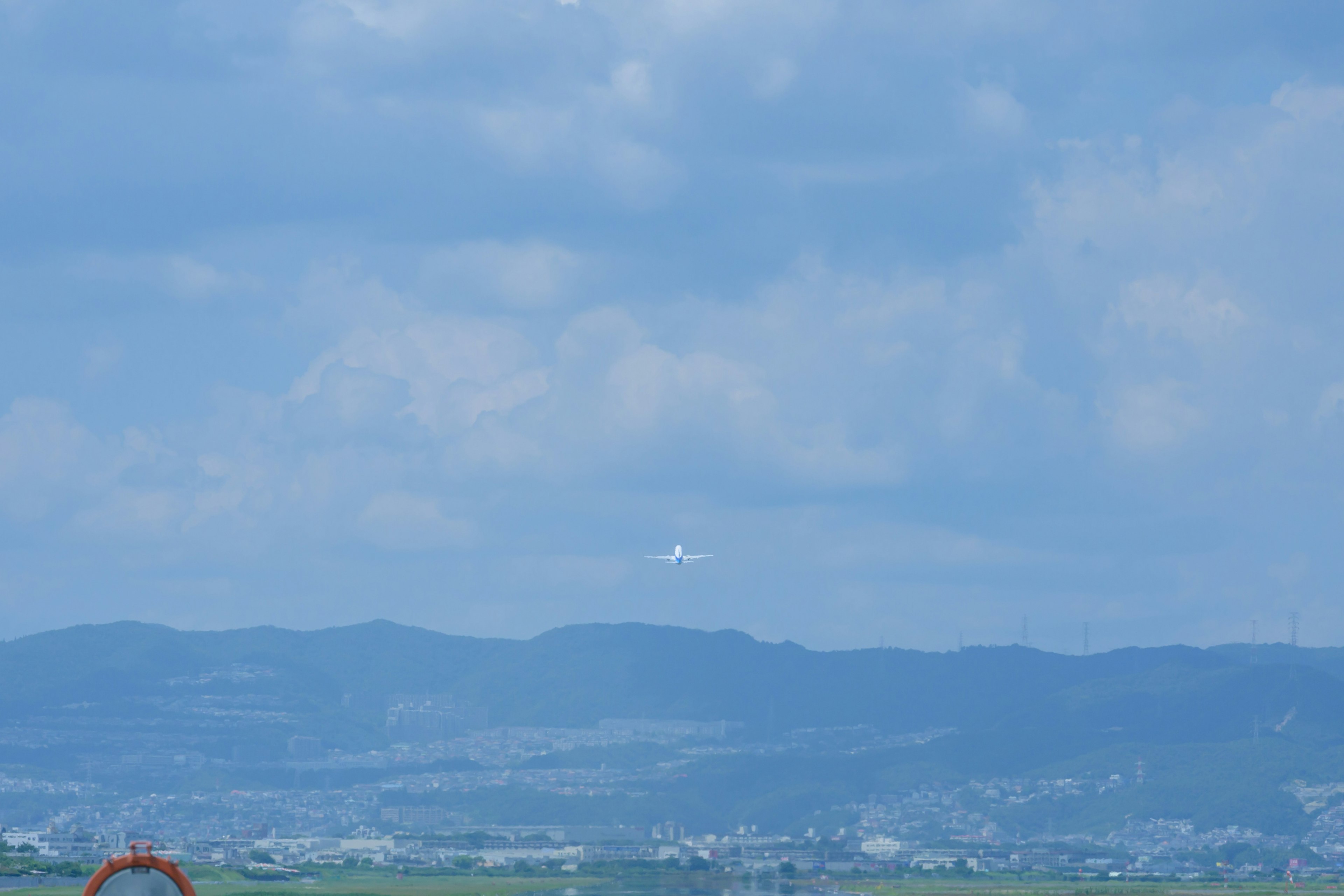 青い空と雲の下に山々が広がり、その上を飛行機が飛んでいる風景