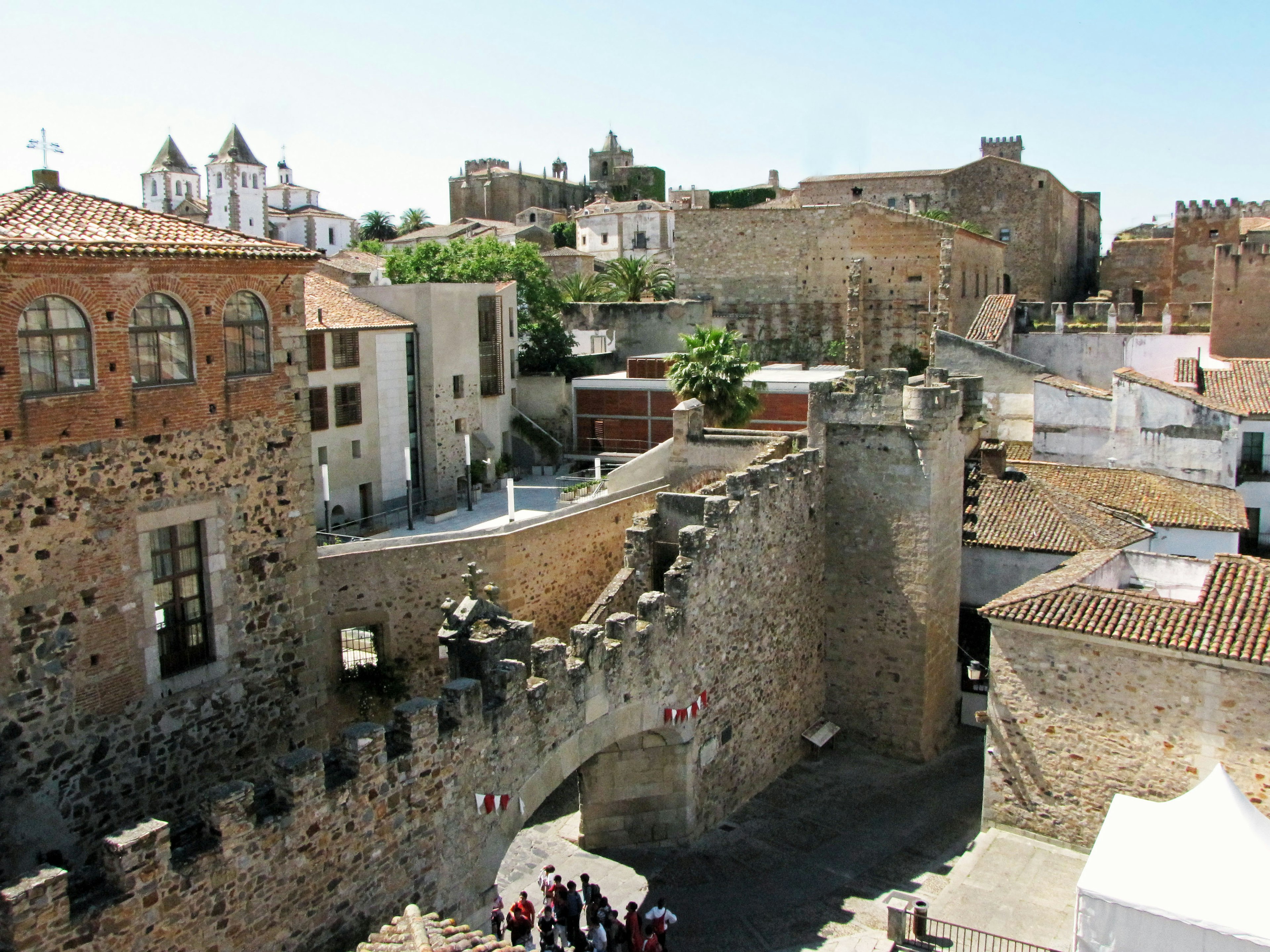 Paesaggio urbano storico con mura in pietra e edifici con persone in una piazza