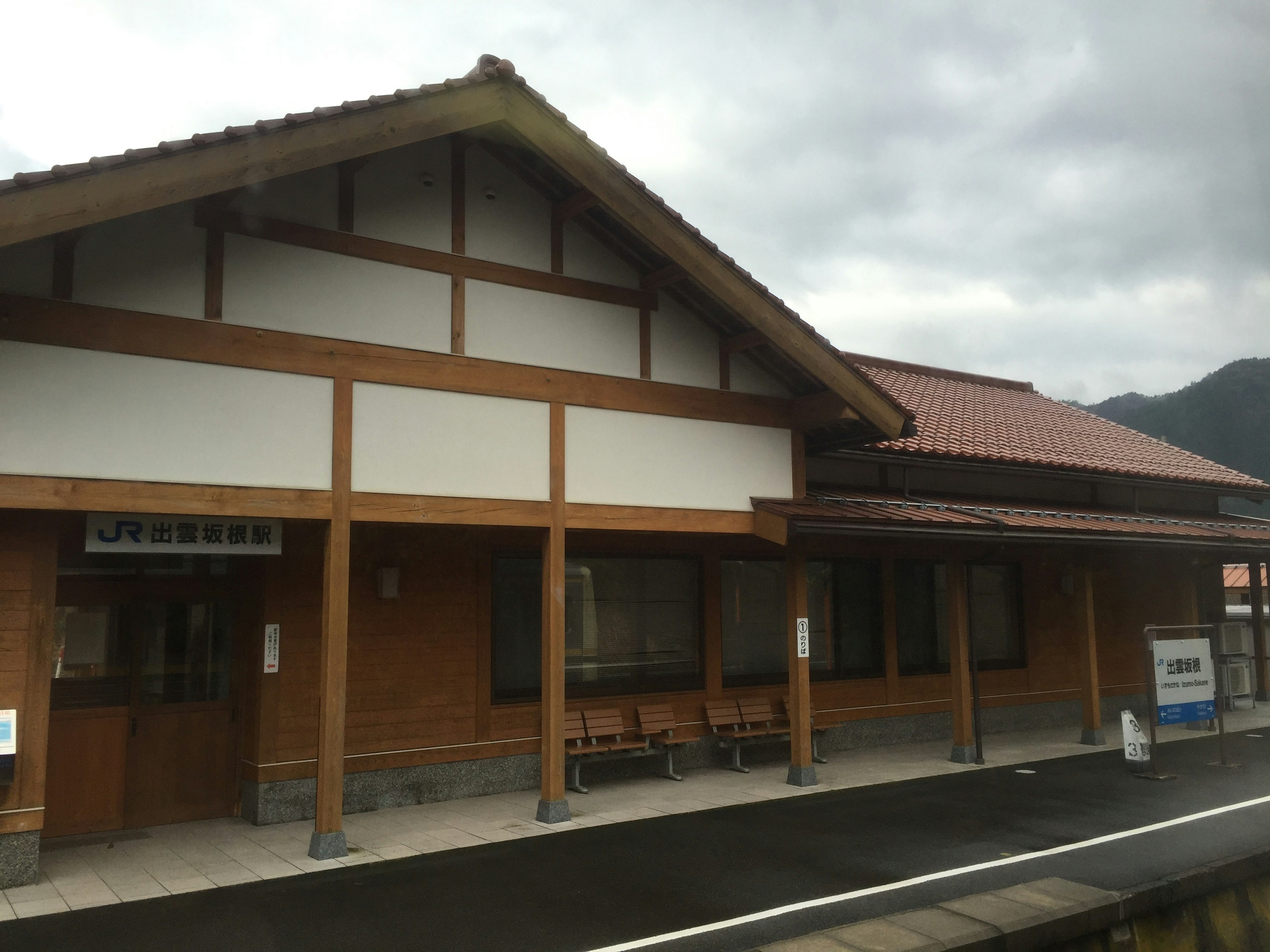 ภายนอกสถานีรถไฟไม้ที่มีหลังคาเอียงและพื้นที่นั่ง