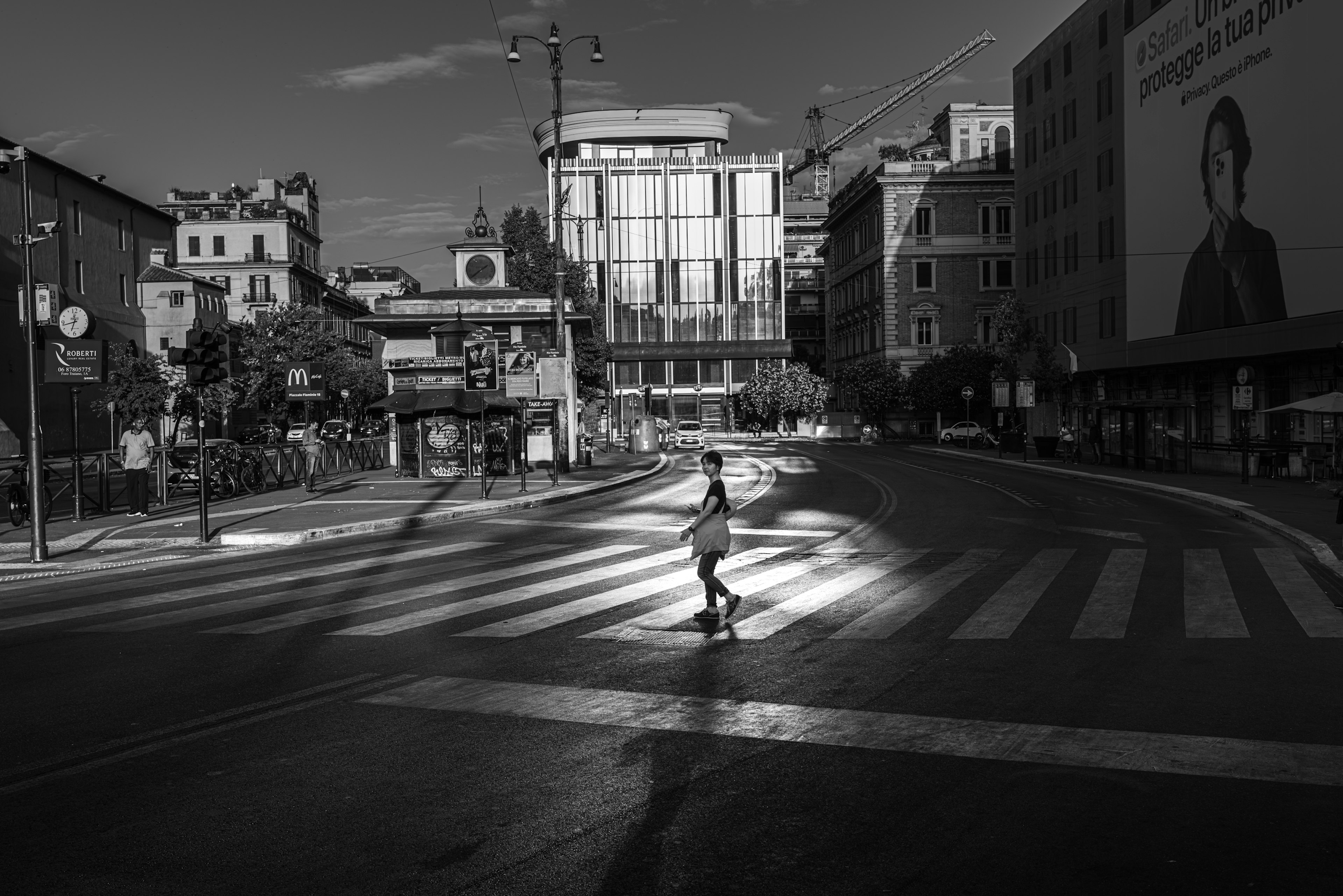 Schatten einer Person, die einen Zebrastreifen in einer schwarz-weißen Stadtstraße überquert Moderne Gebäude und eine Werbung im Hintergrund