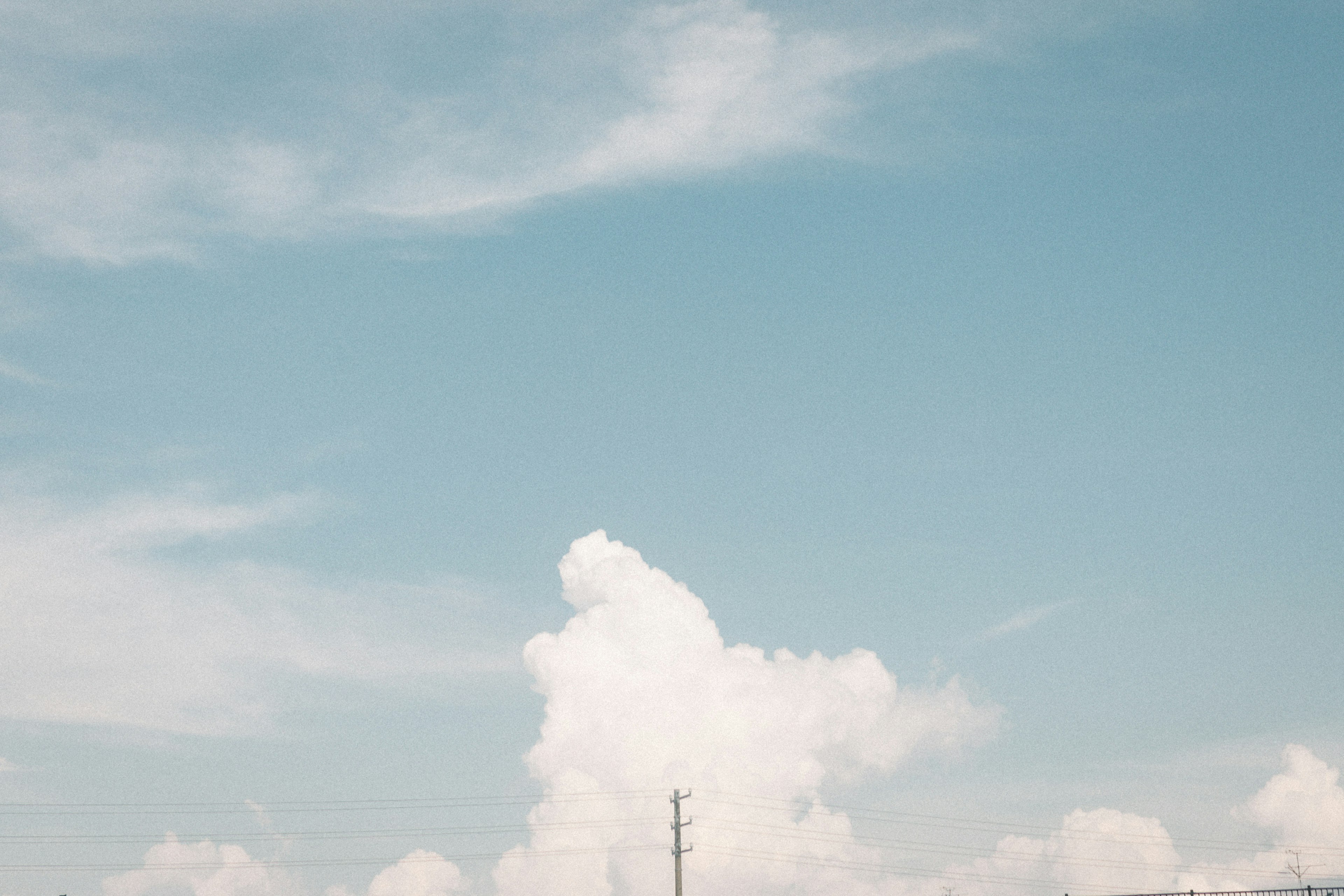 Awan putih di langit biru dengan siluet tiang listrik