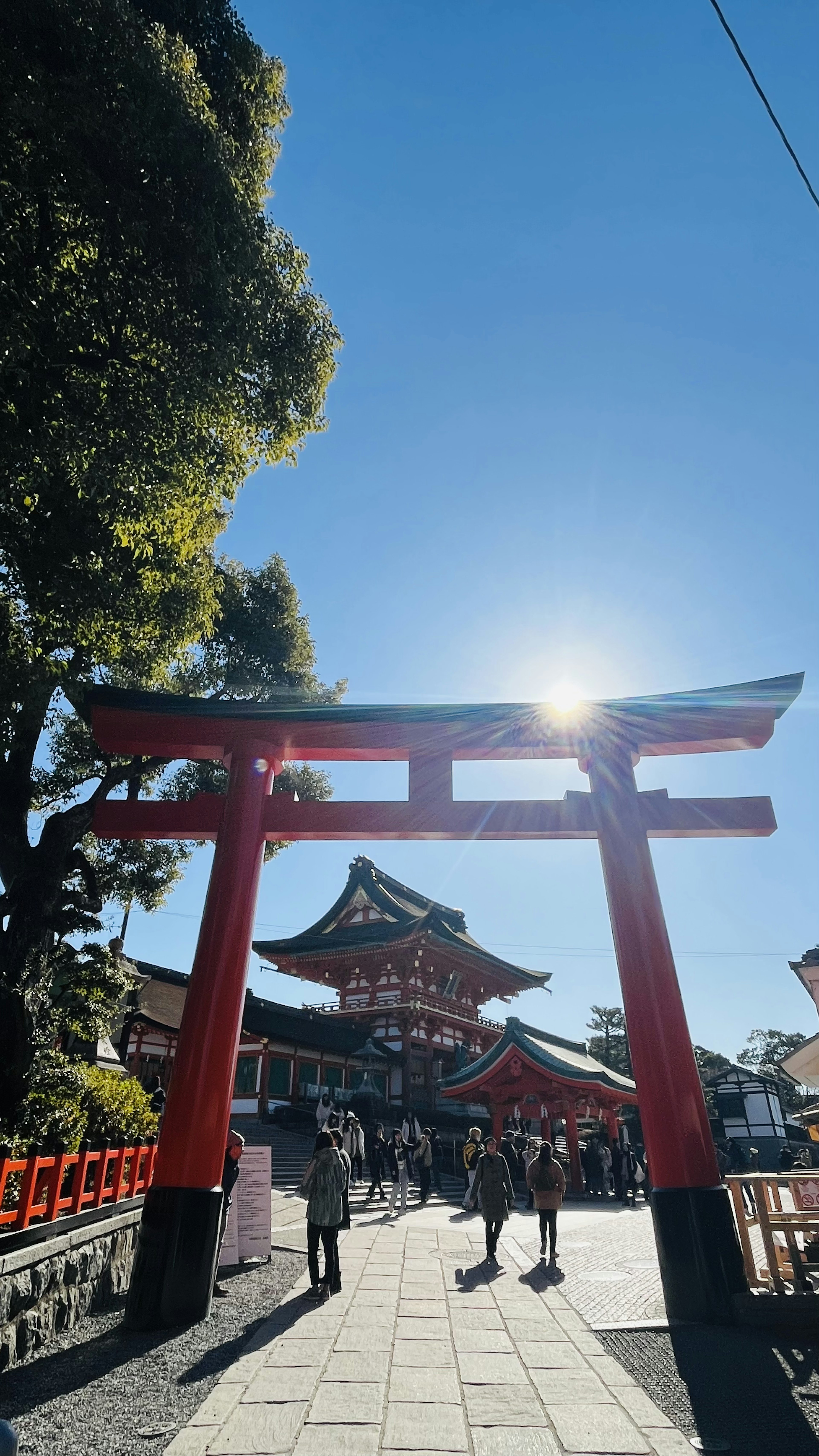 Puerta torii roja con un santuario al fondo bajo un cielo azul despejado