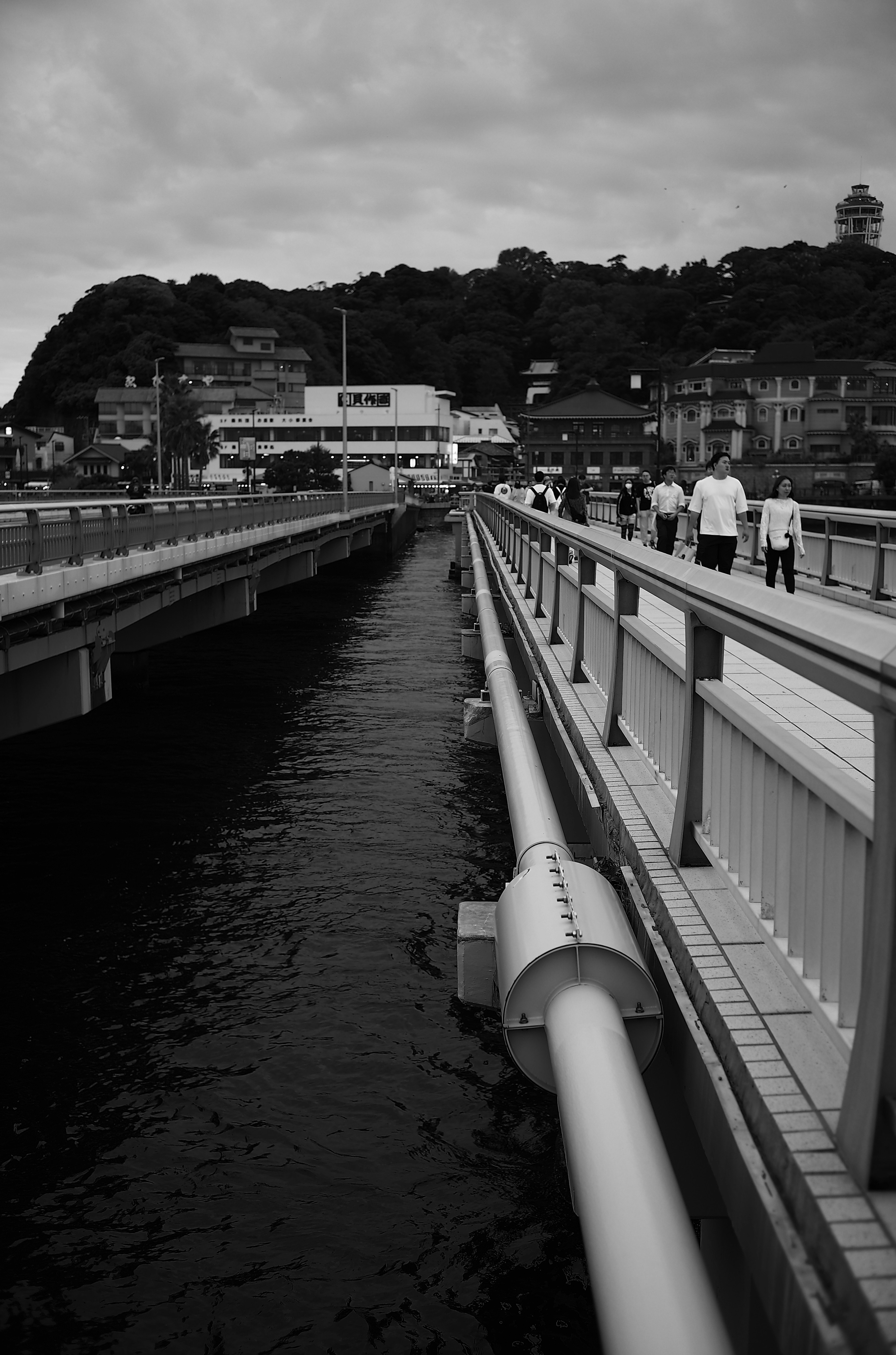 Image en noir et blanc d'un pont le long d'un cours d'eau avec des personnes marchant