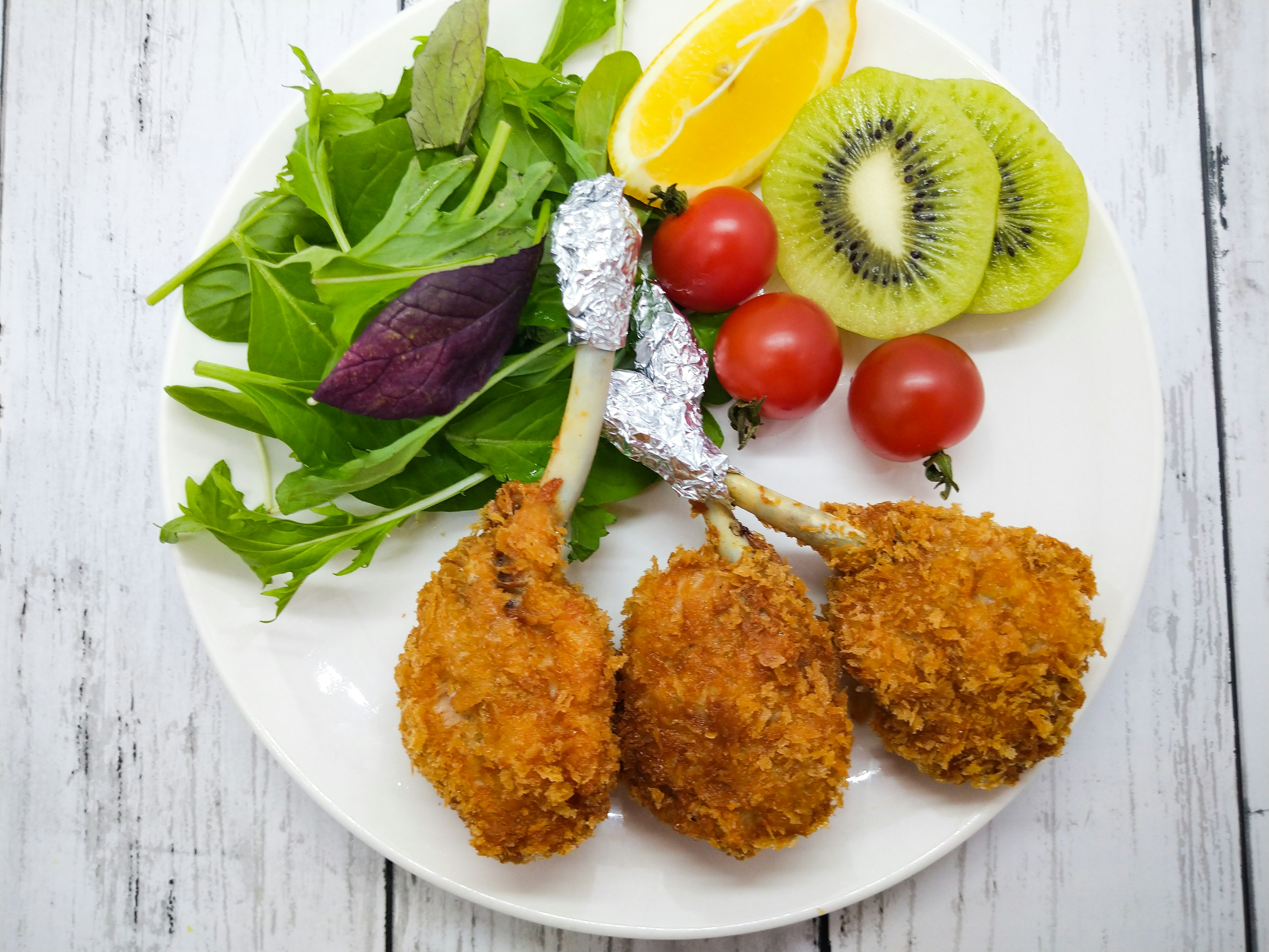 Three fried chicken legs on a plate with salad and fruit