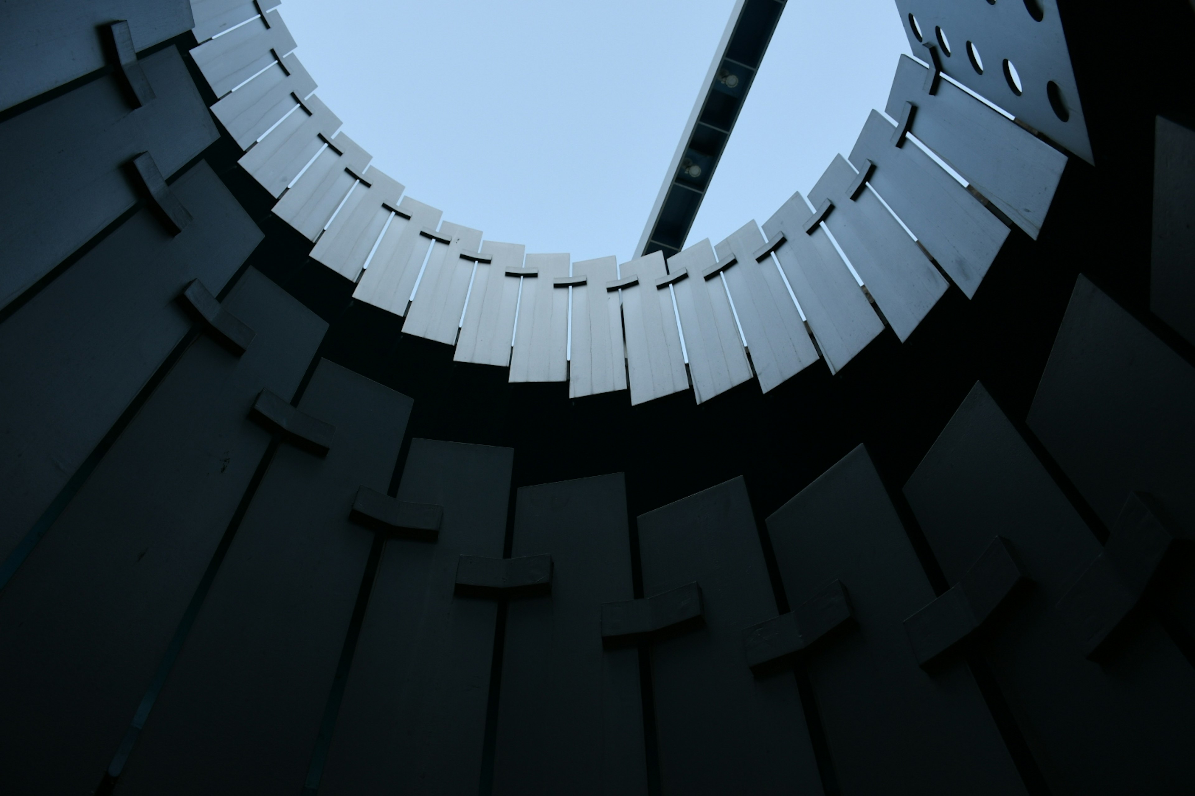 Vue de l'intérieur d'une structure circulaire en regardant vers le ciel bleu avec des murs noirs contrastants