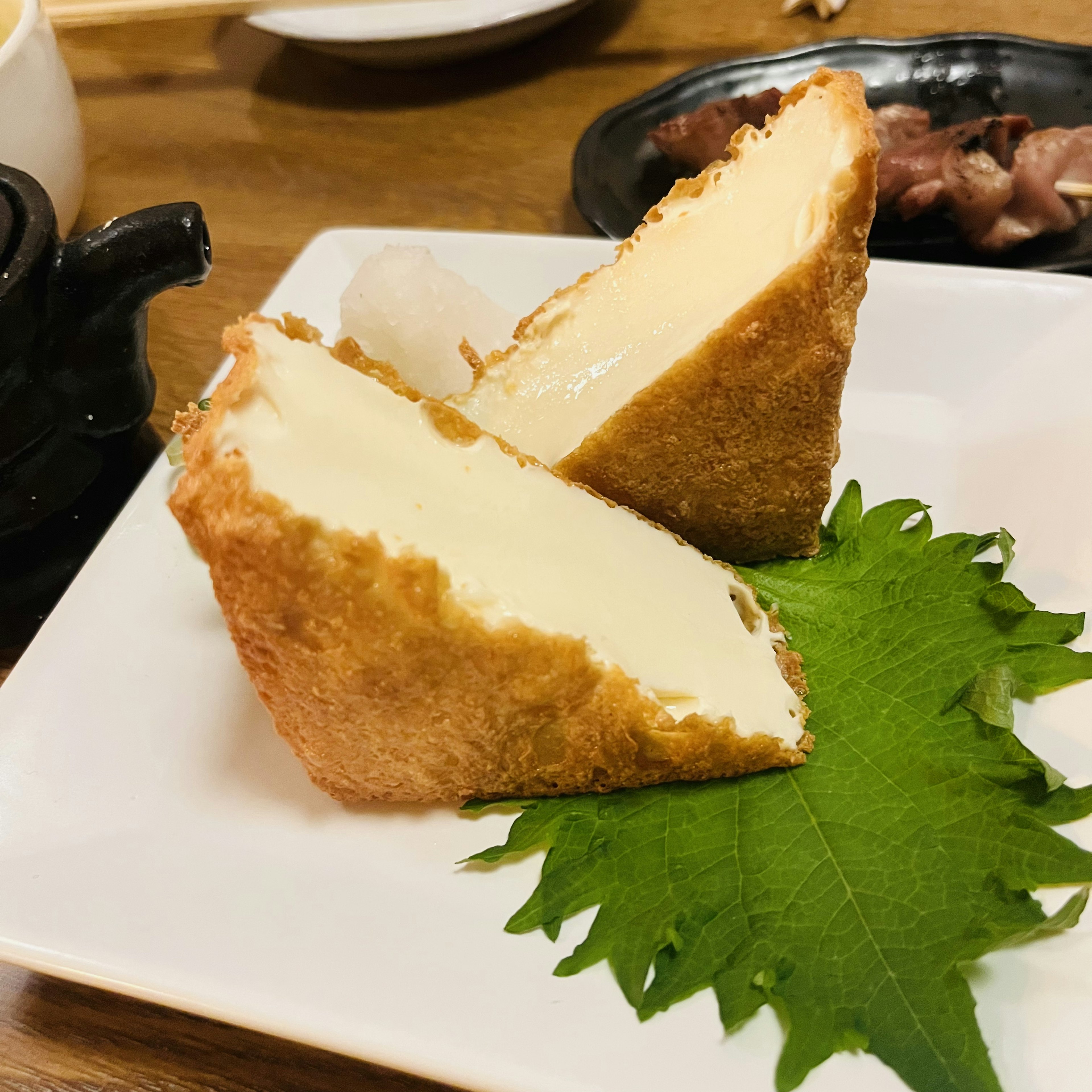 Due pezzi di tofu fritto con ripieno cremoso serviti su un piatto bianco con una foglia verde