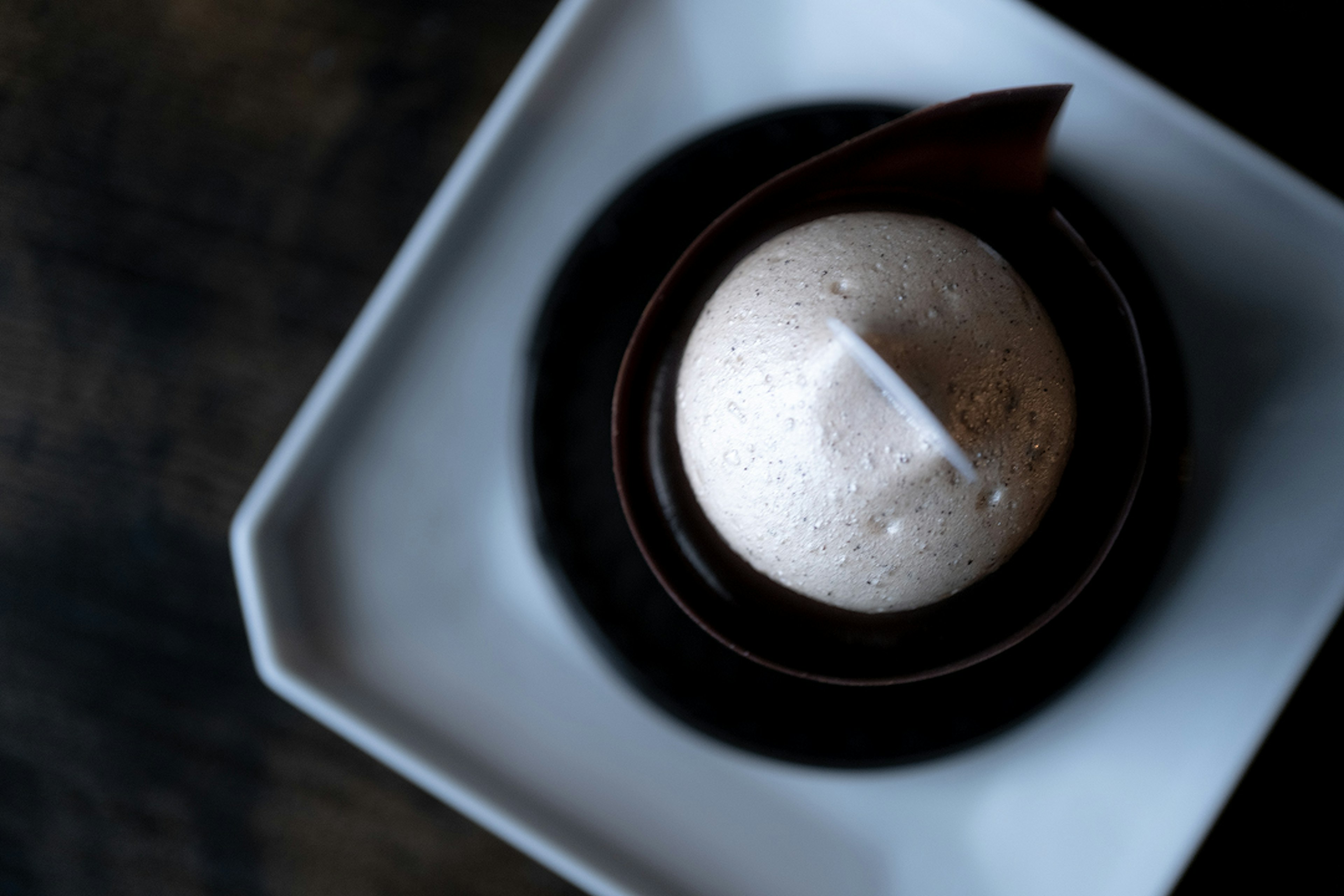 Vista superior de un postre con una esfera blanca en un plato de chocolate negro