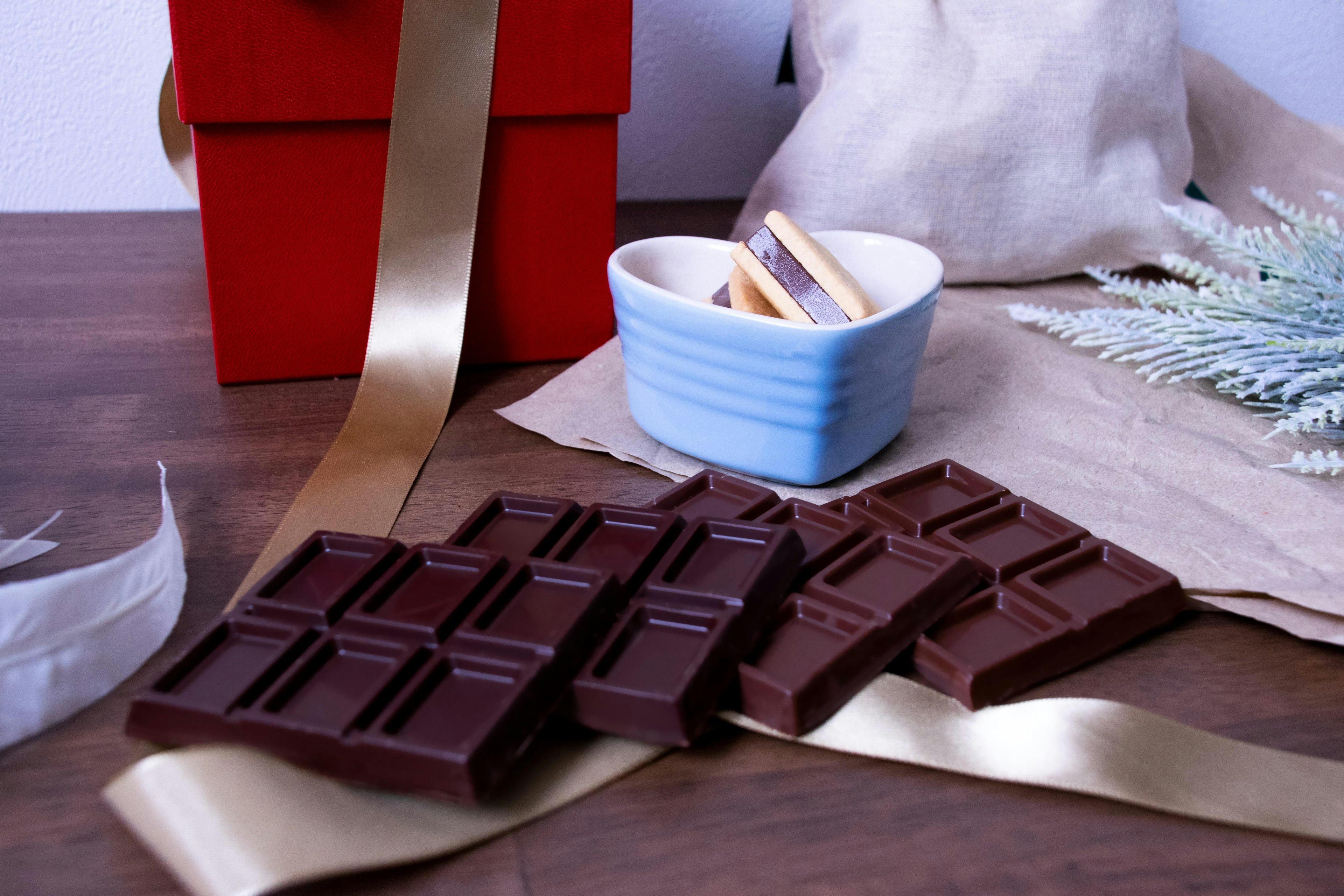 A red gift box next to chocolate bars on a table with a blue dish and ribbon