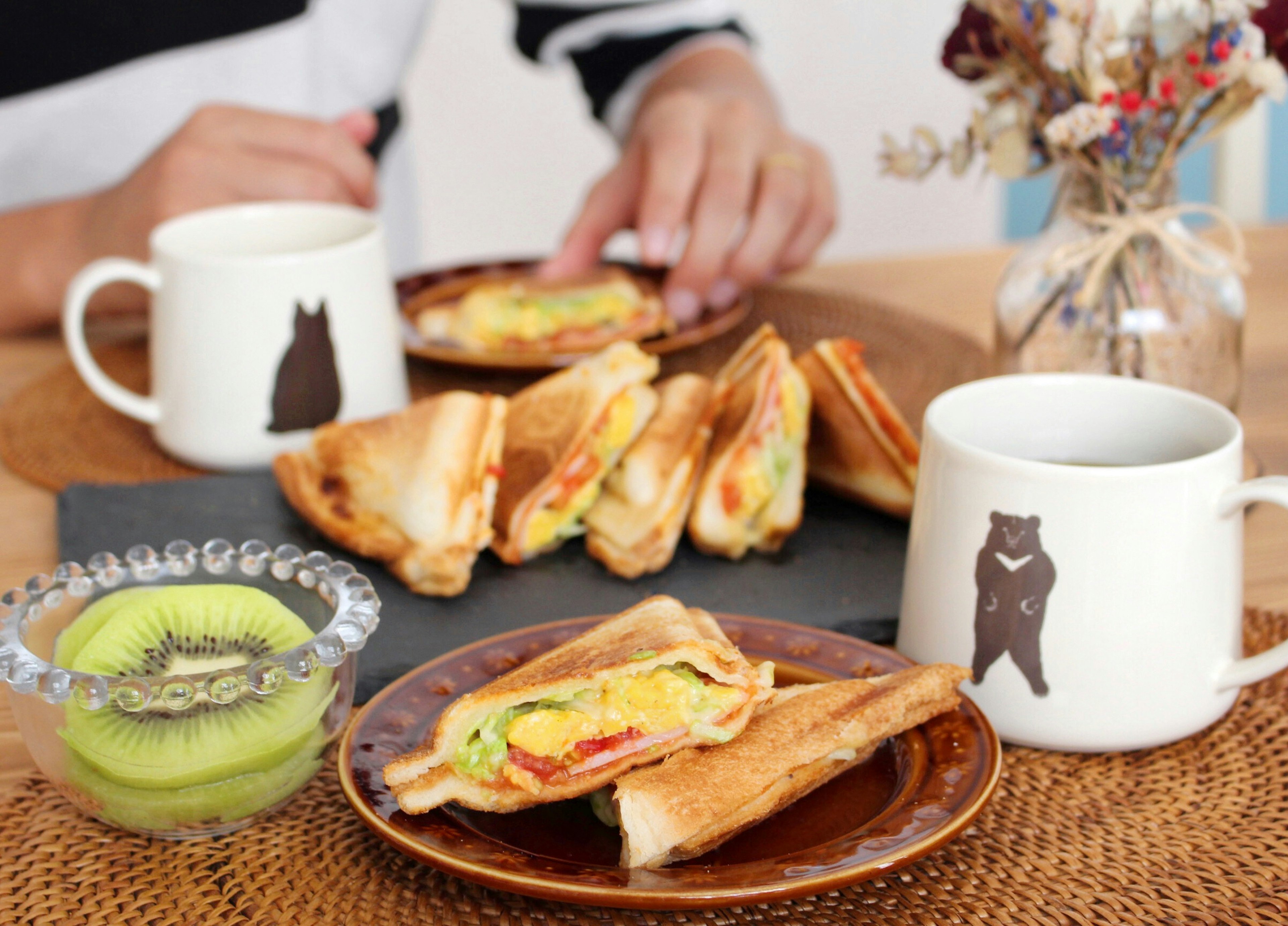 A table setting featuring sandwiches and drinks A green fruit dessert is in the foreground Two mugs with bear illustrations