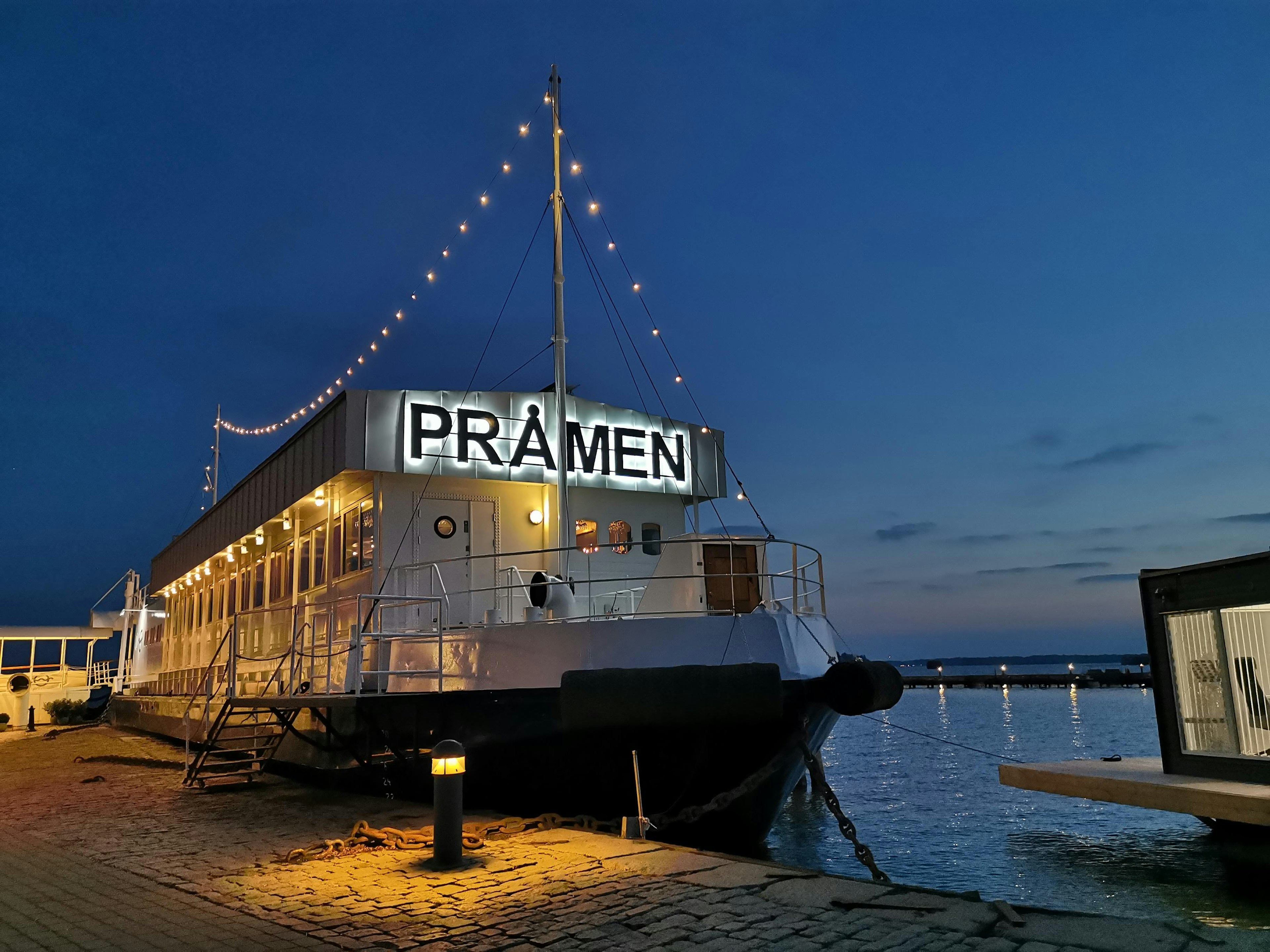 Restaurant boat named Pramen illuminated at night with decorative lights