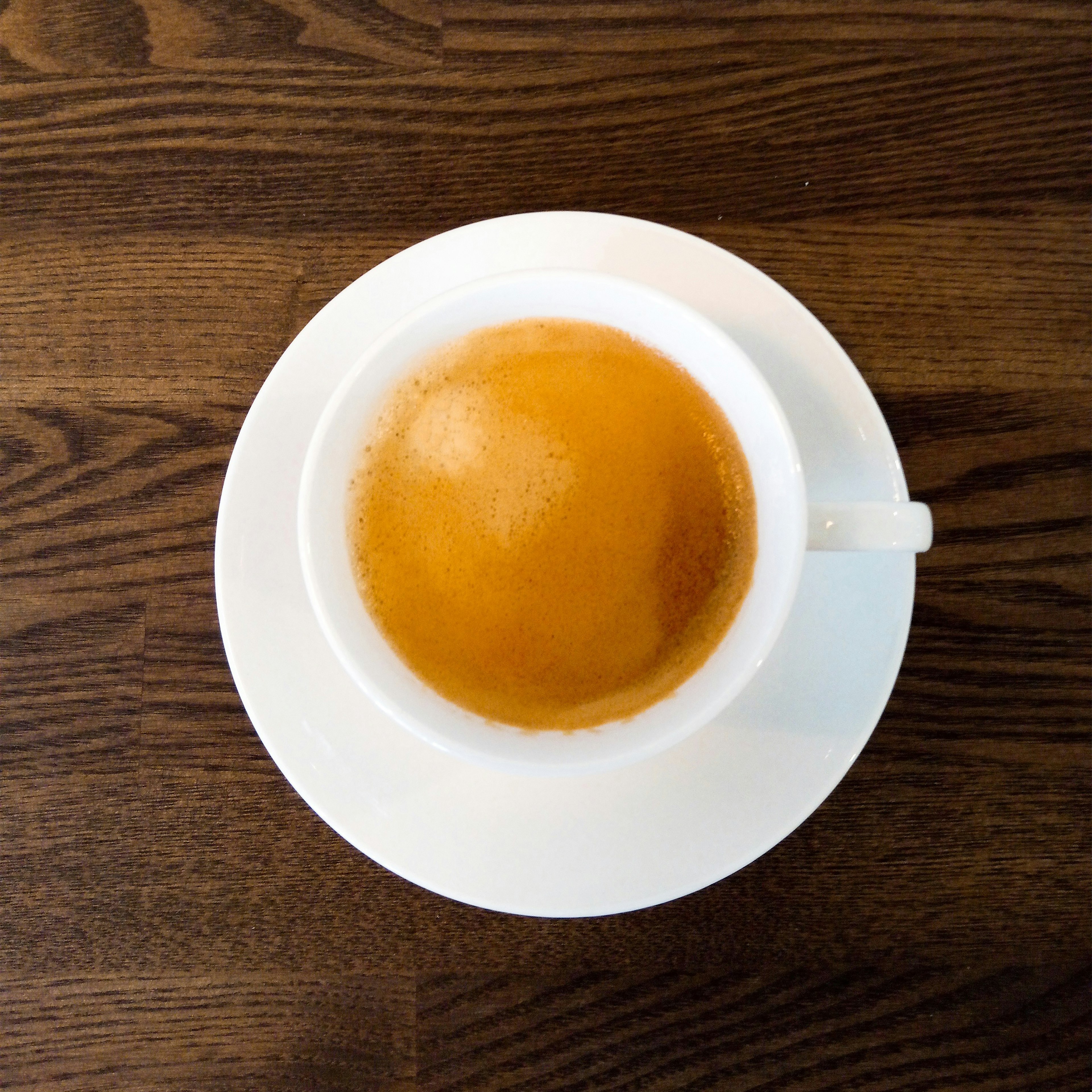 Vista superior de un espresso en una taza blanca sobre una mesa de madera