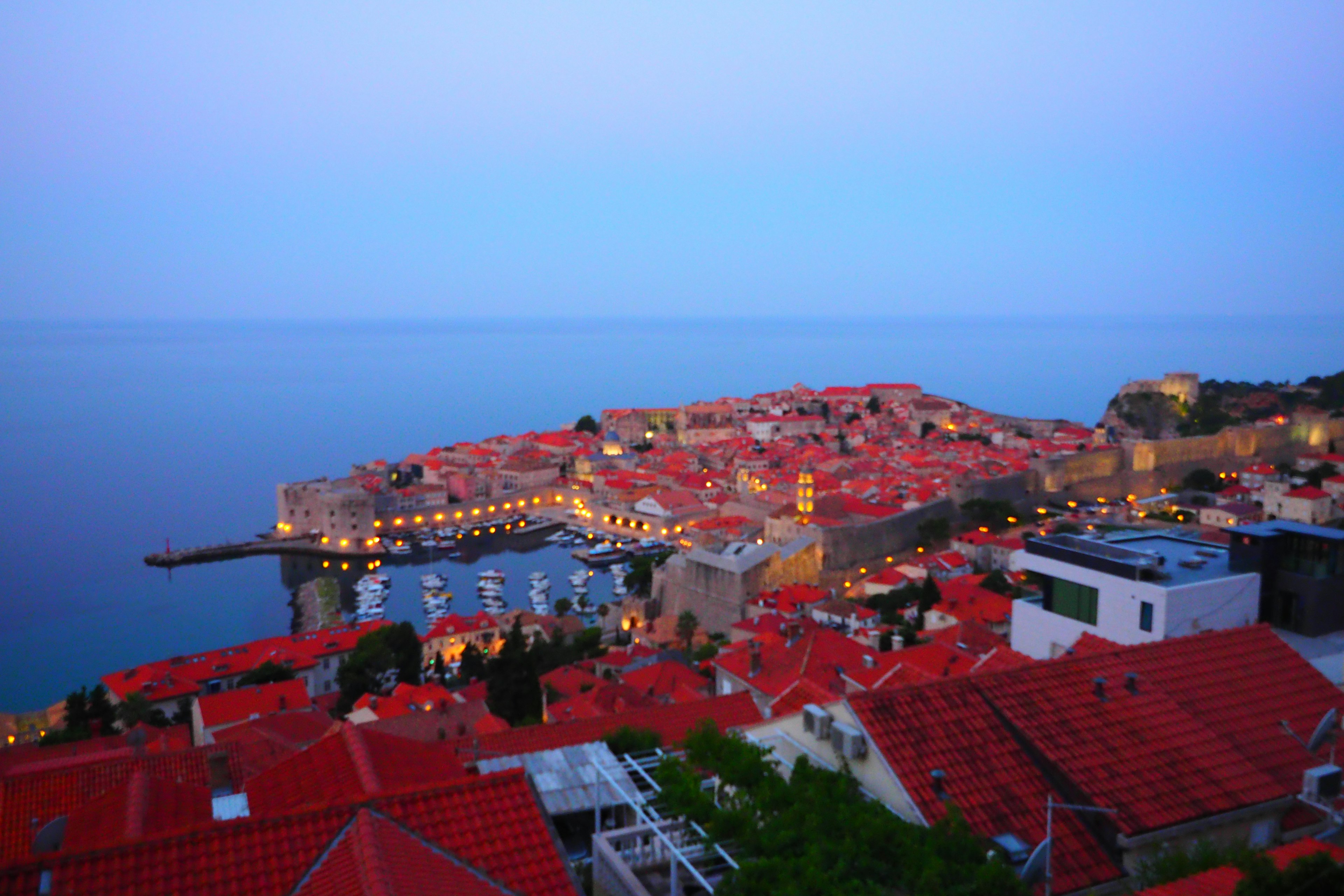 A beautiful view of Dubrovnik's coastline with red-roofed houses under a blue sky at dusk