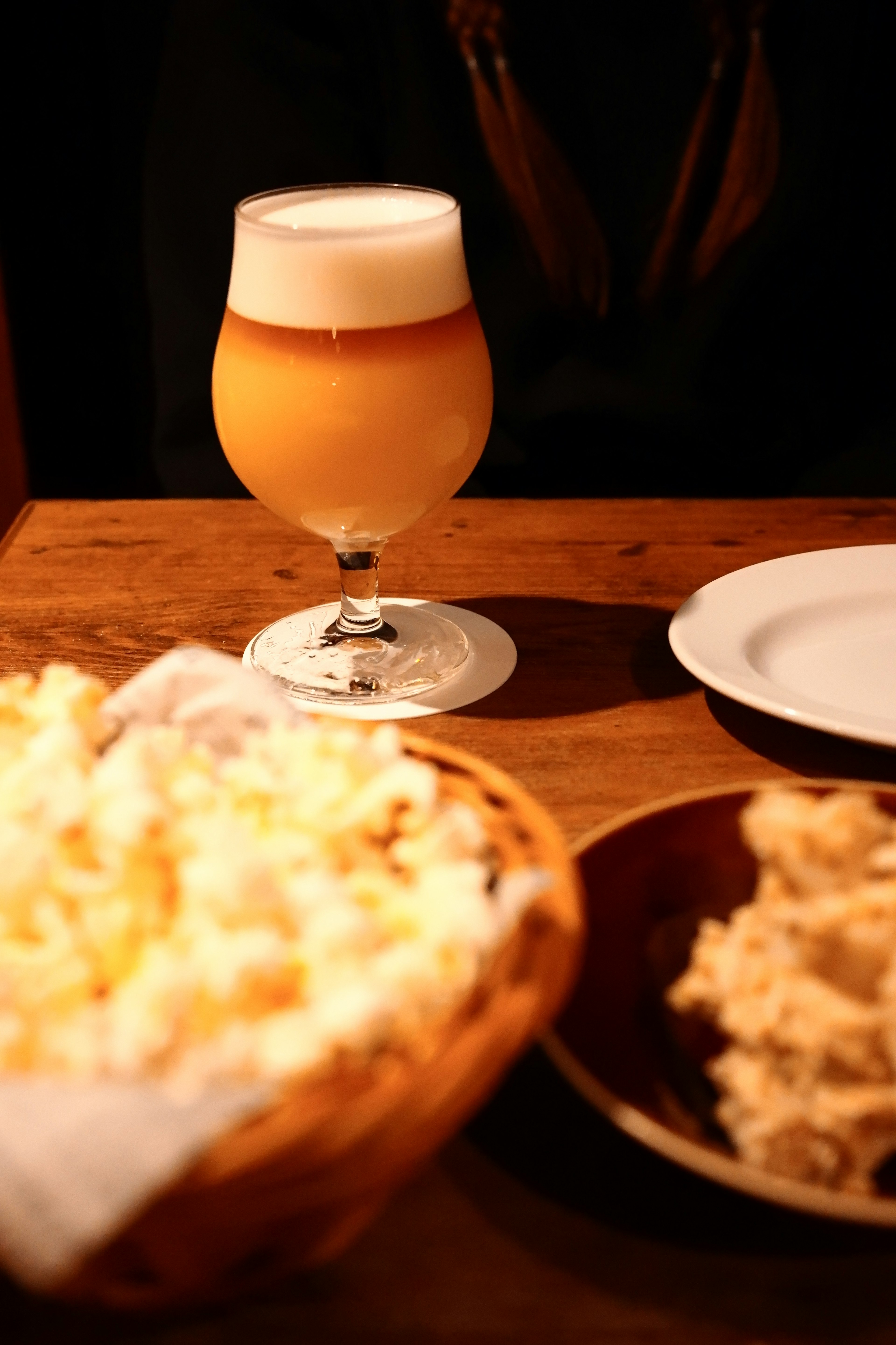 Un verre de bière avec de la mousse à côté d'un panier de pop-corn sur une table en bois