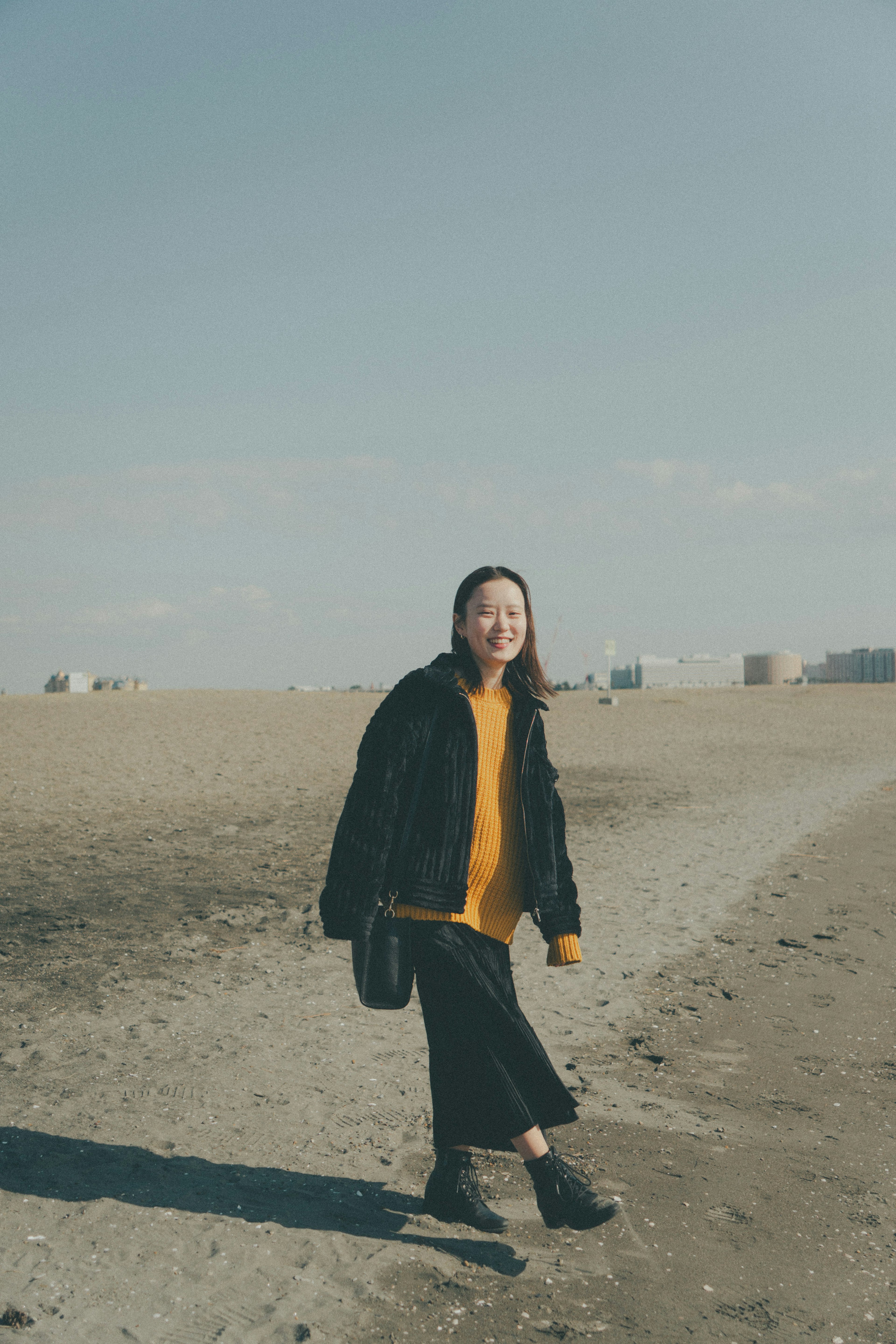 Eine Frau, die am Strand spaziert, trägt eine schwarze Jacke und einen gelben Pullover