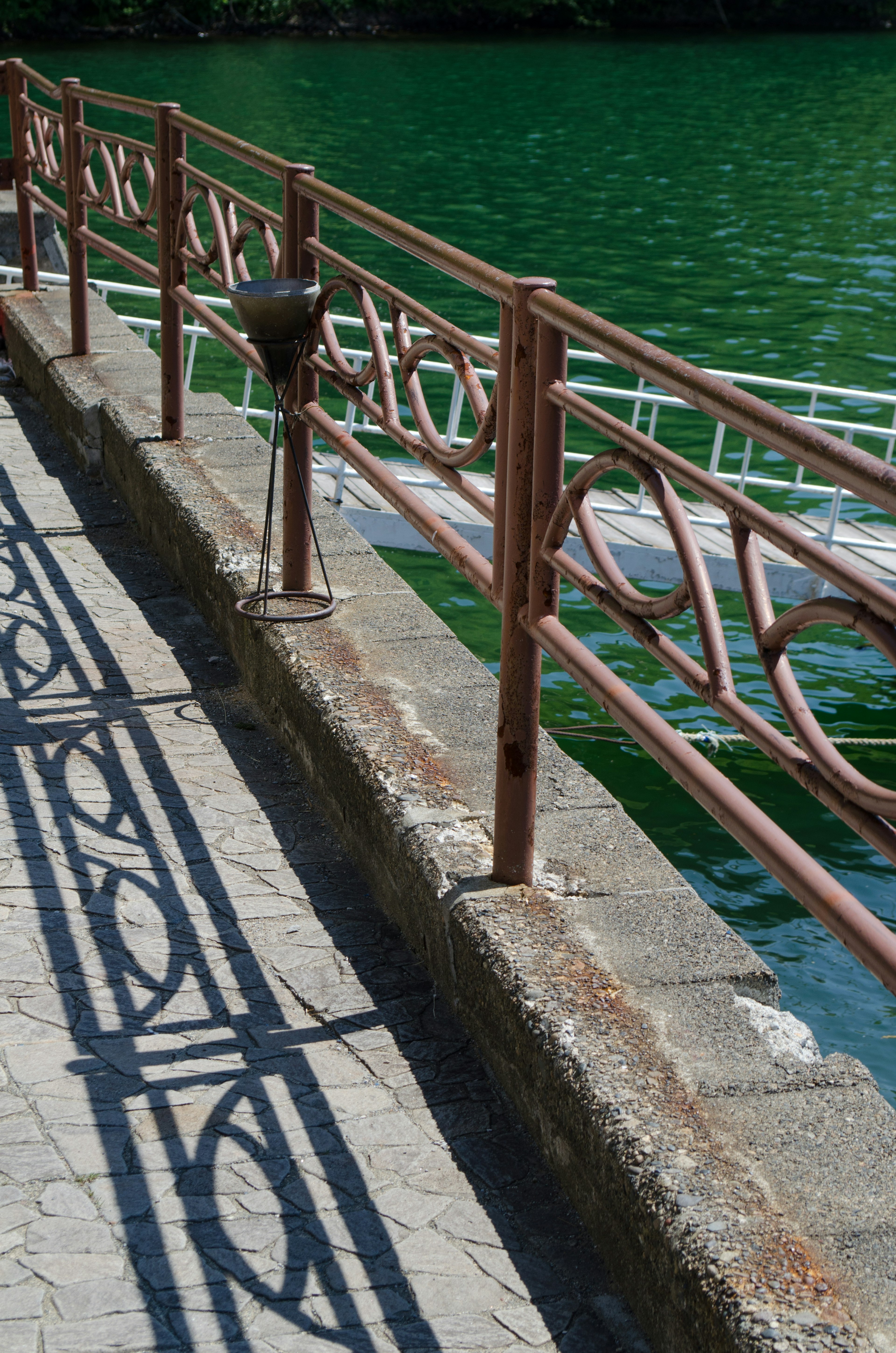 Garde-corps décoratif projetant des ombres sur l'eau verte au bord de la rivière