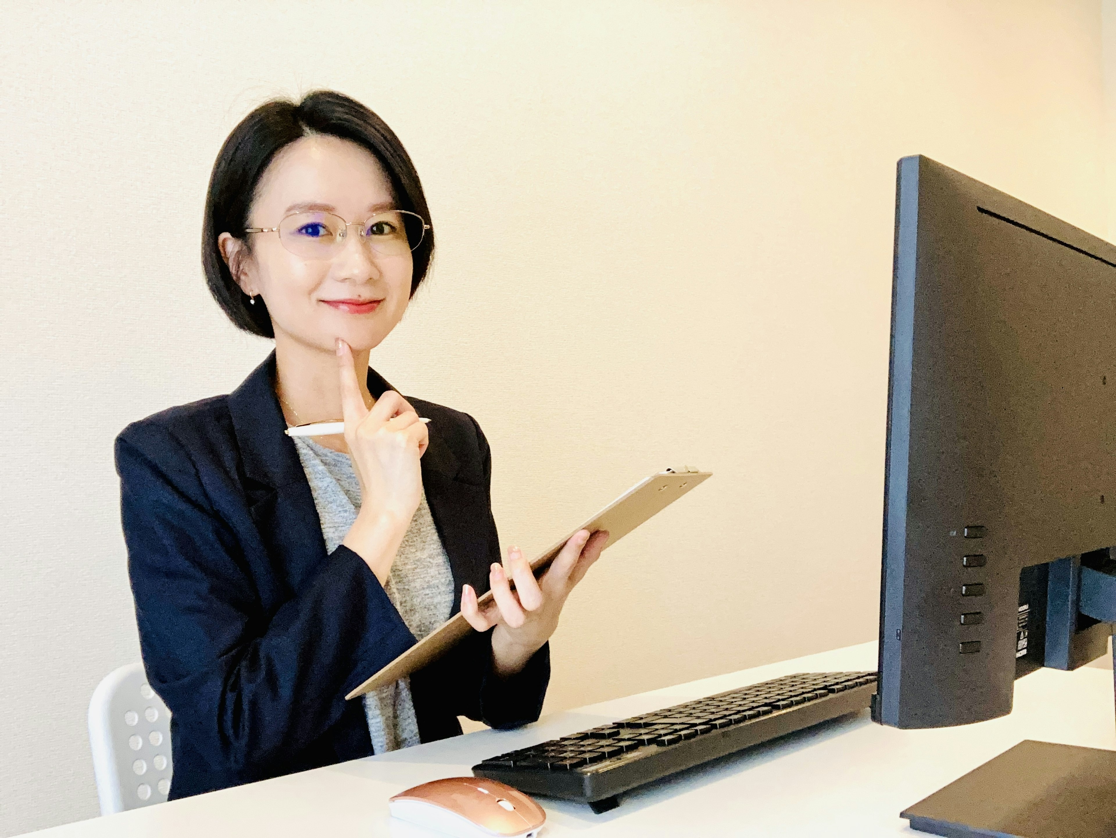 Businesswoman in an office deep in thought holding a clipboard while seated at a computer