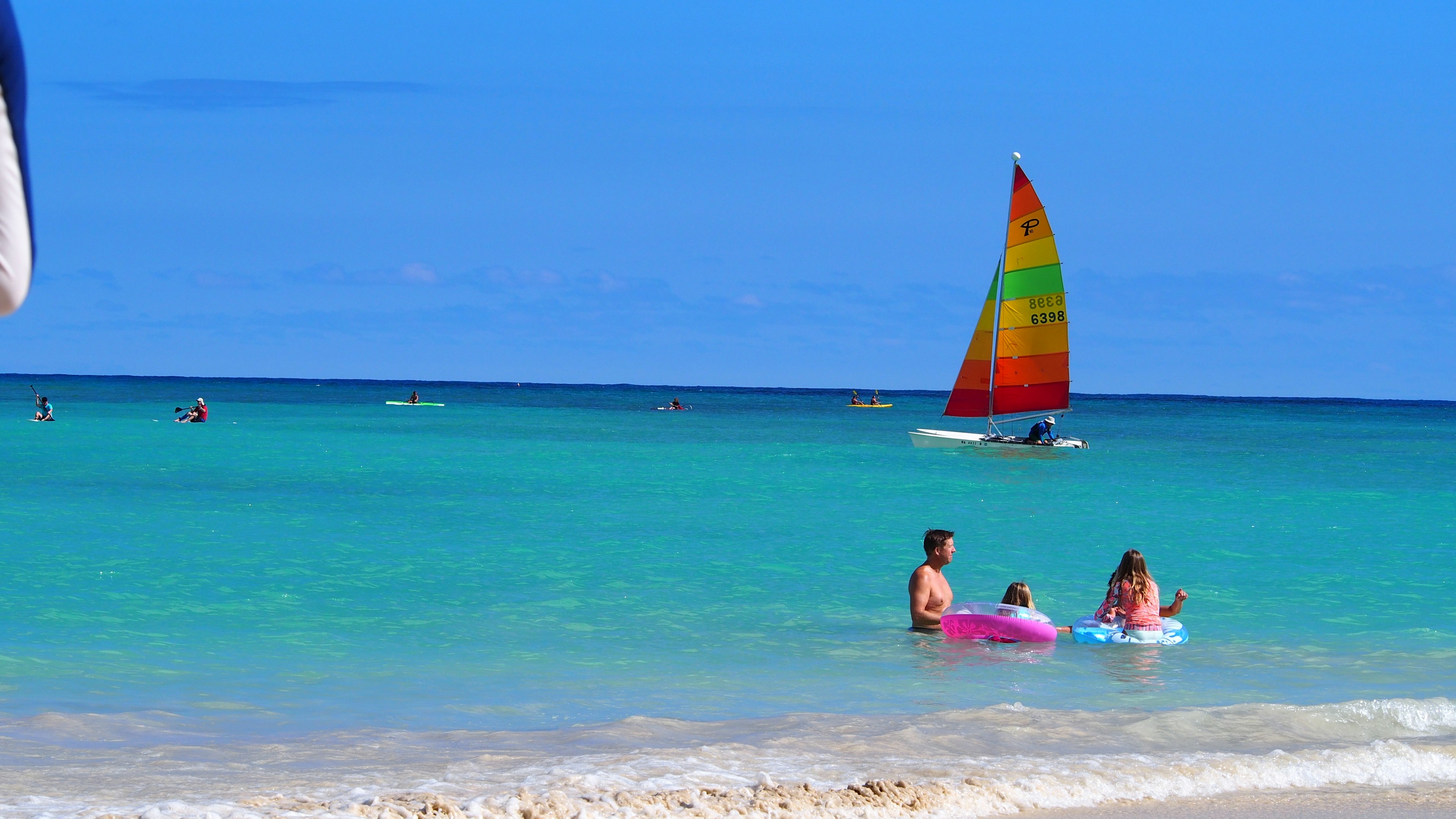 Family playing in the blue ocean and beach with a colorful sailboat