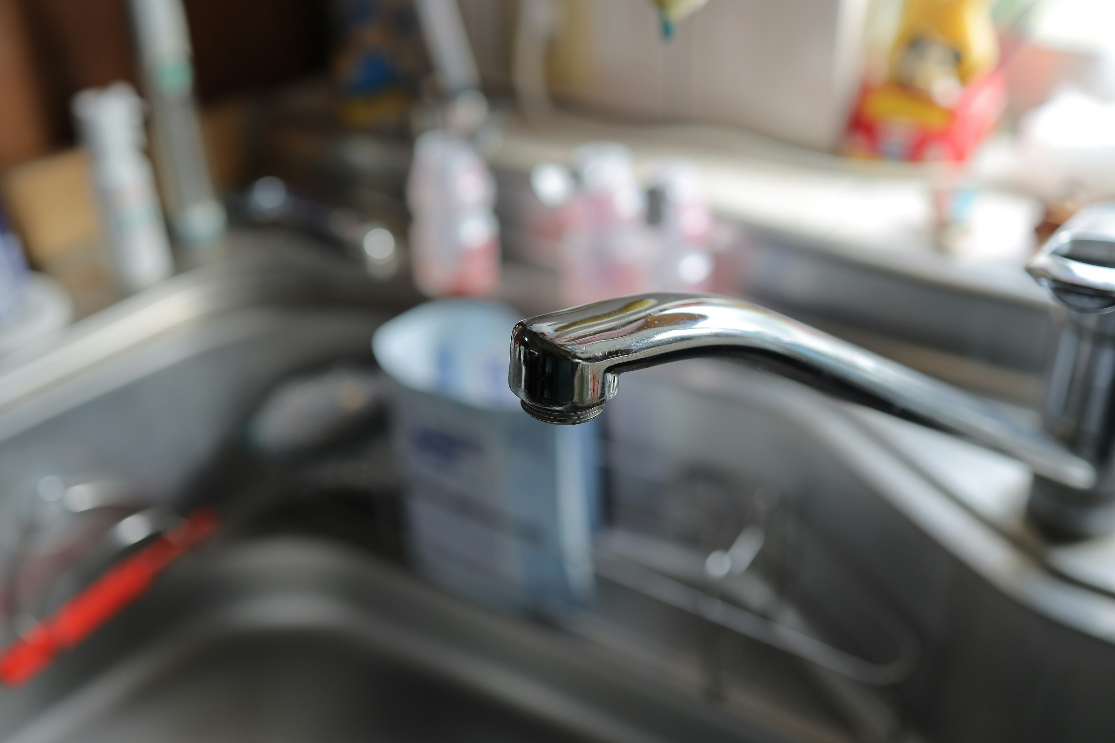 Close-up of a kitchen faucet with various cleaning product bottles in the background