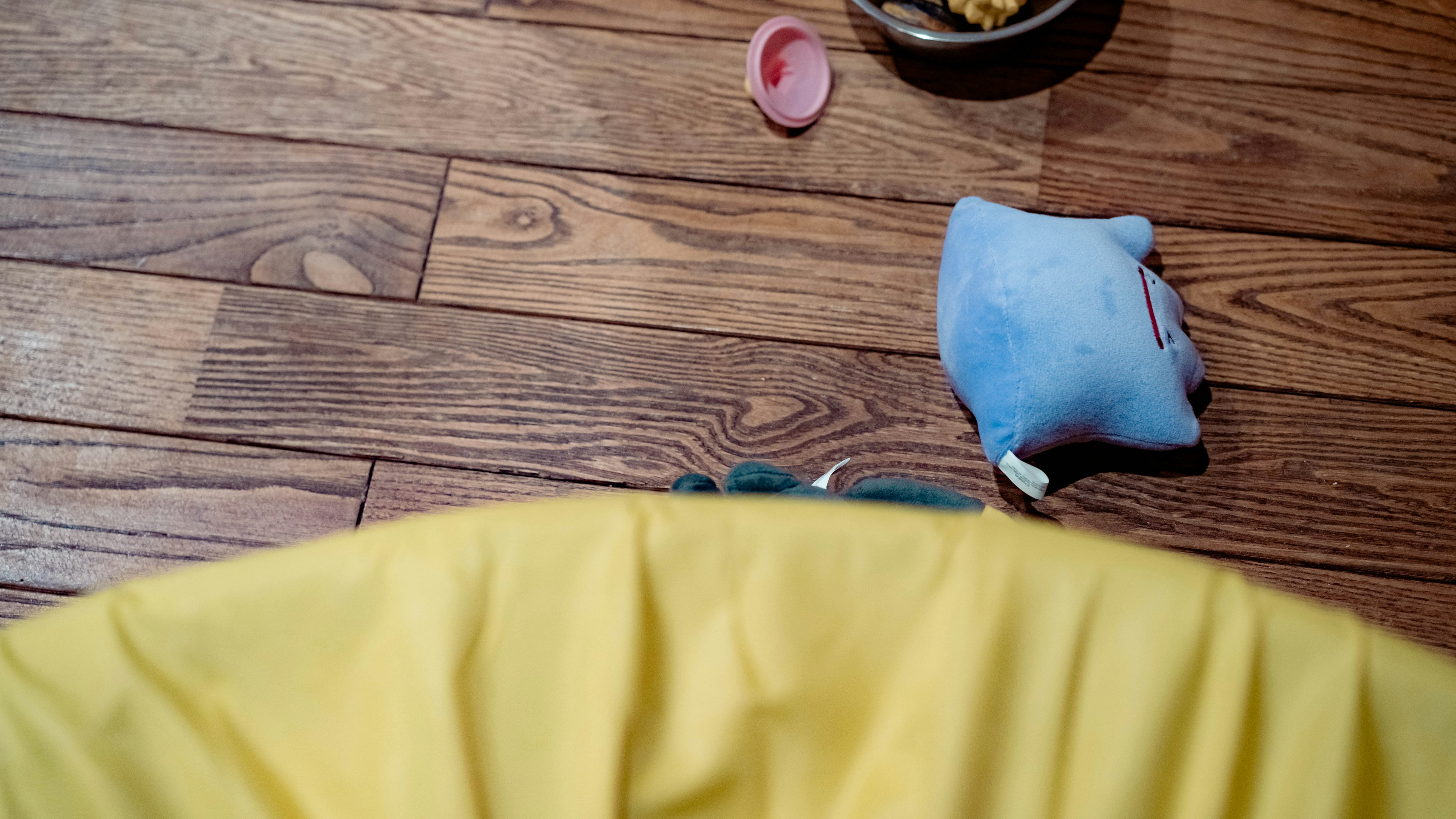 Scène d'un sol avec une couverture jaune un jouet en peluche bleu et un objet rose