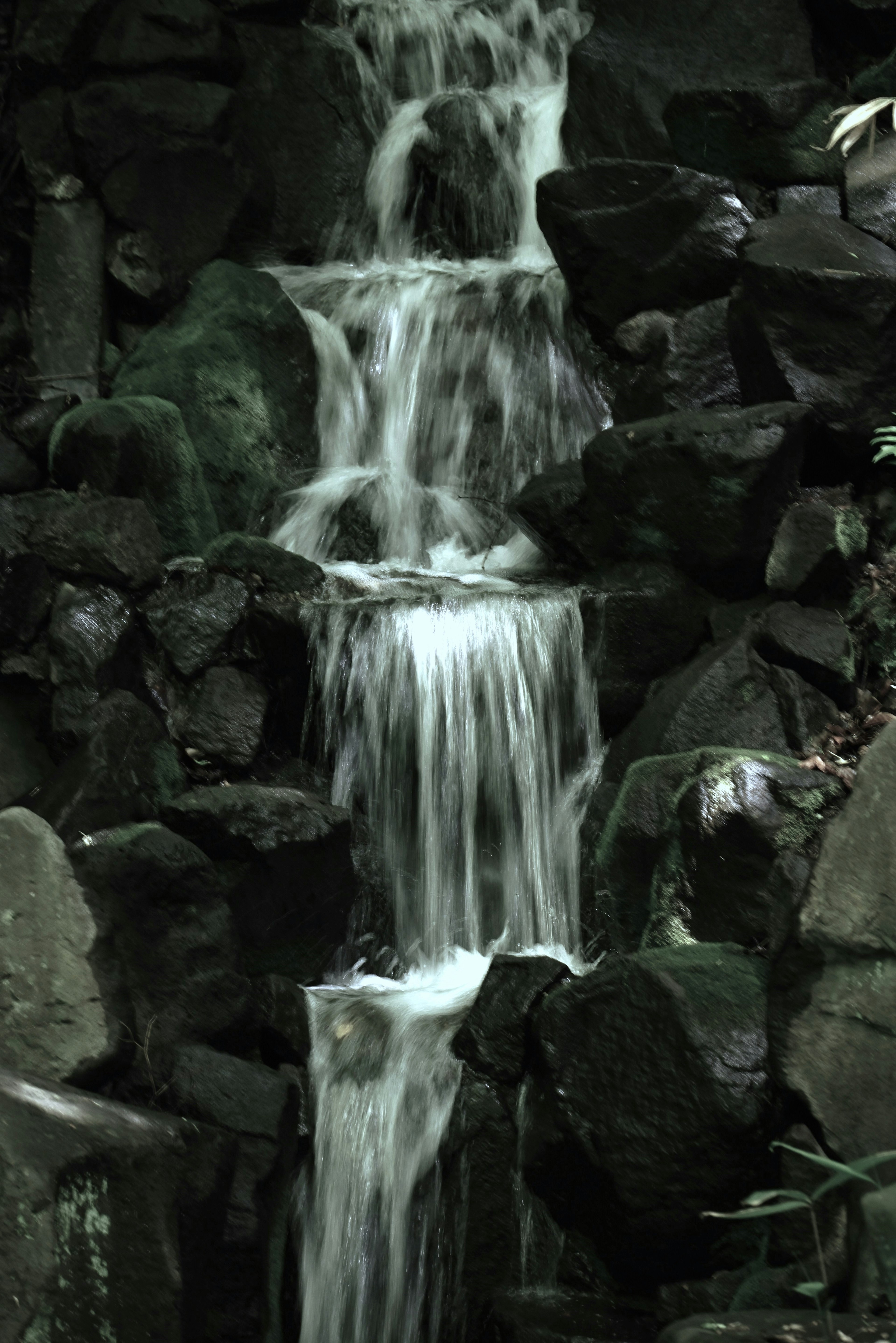 Air mengalir di antara batu gelap dalam air terjun yang tenang