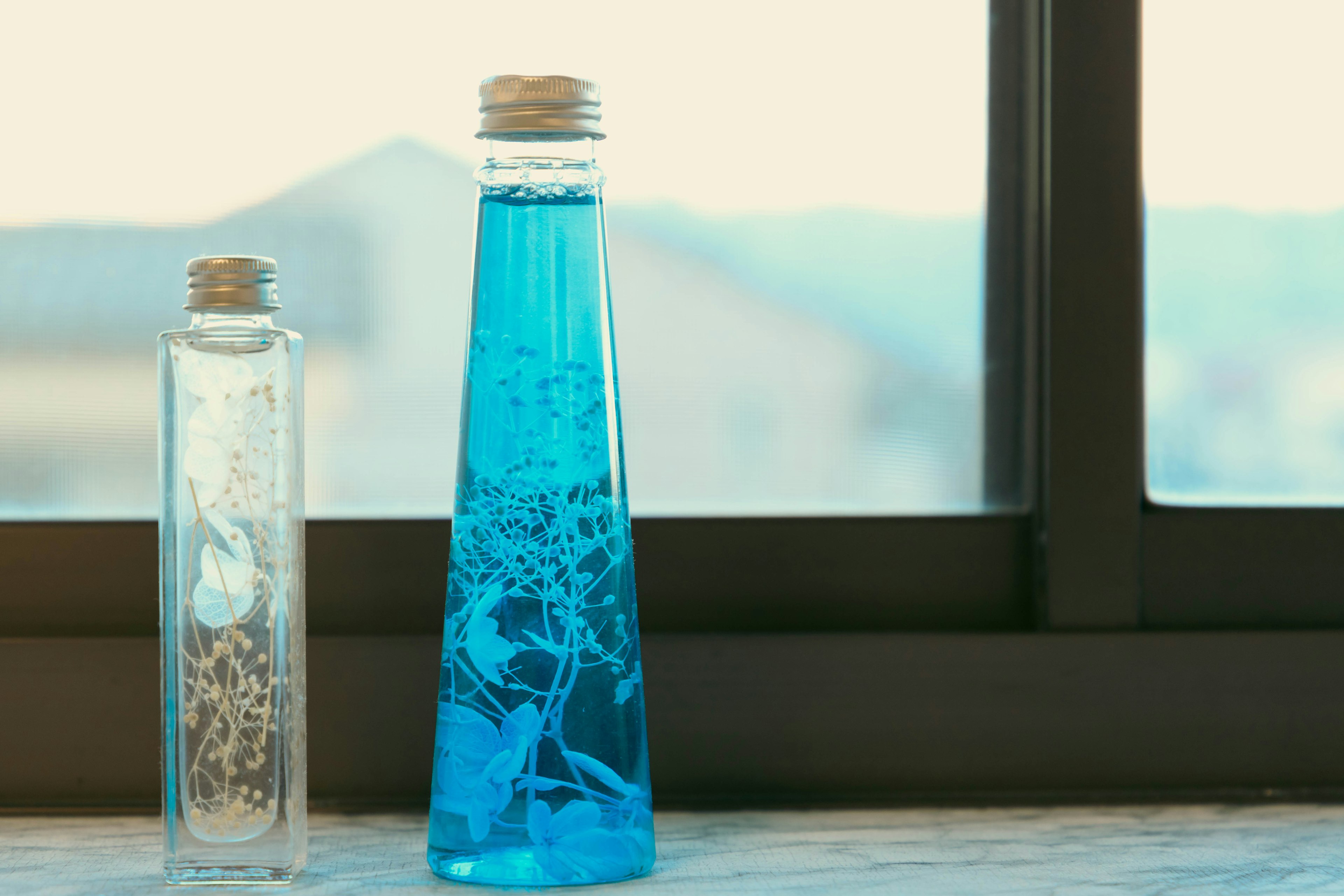 A glass bottle with blue liquid and a clear bottle are placed by a window