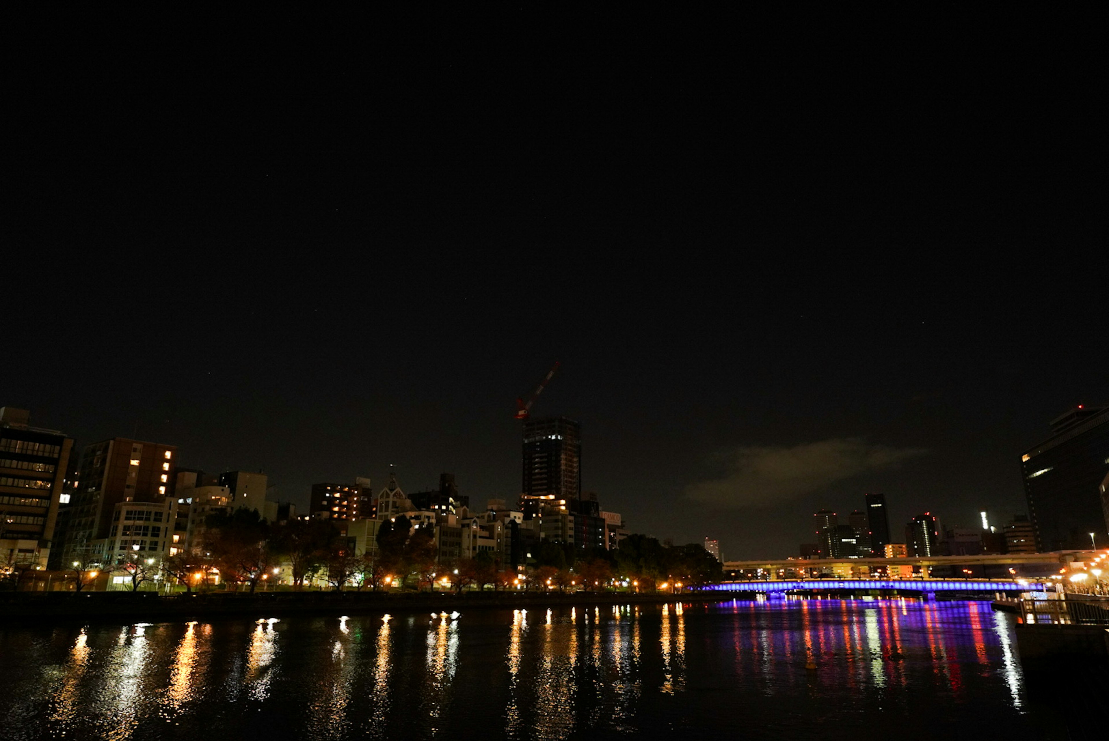 Paisaje urbano nocturno reflejado en el río con rascacielos iluminados y luces coloridas del puente