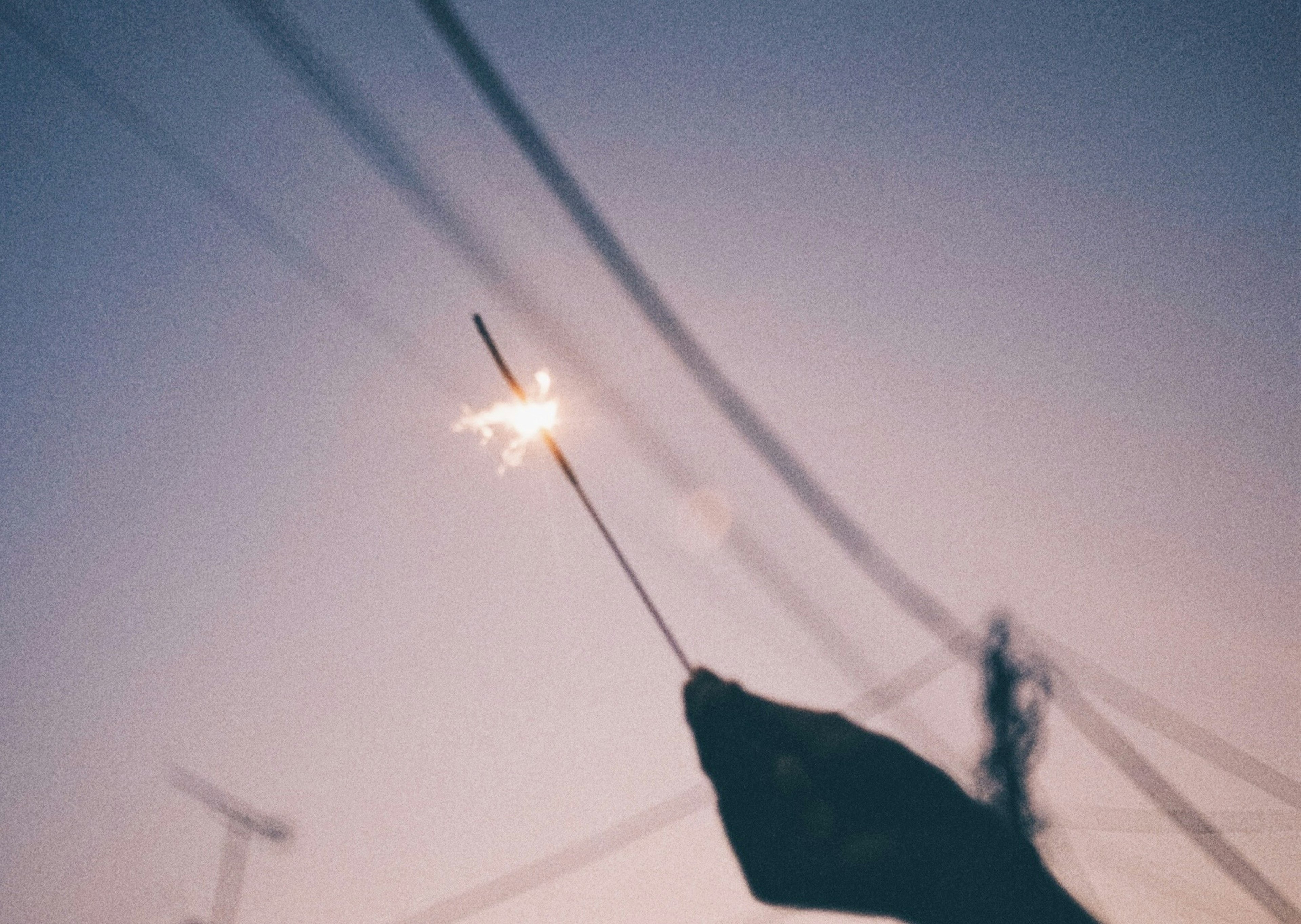 A silhouette of a hand holding a sparkler glowing against a twilight sky