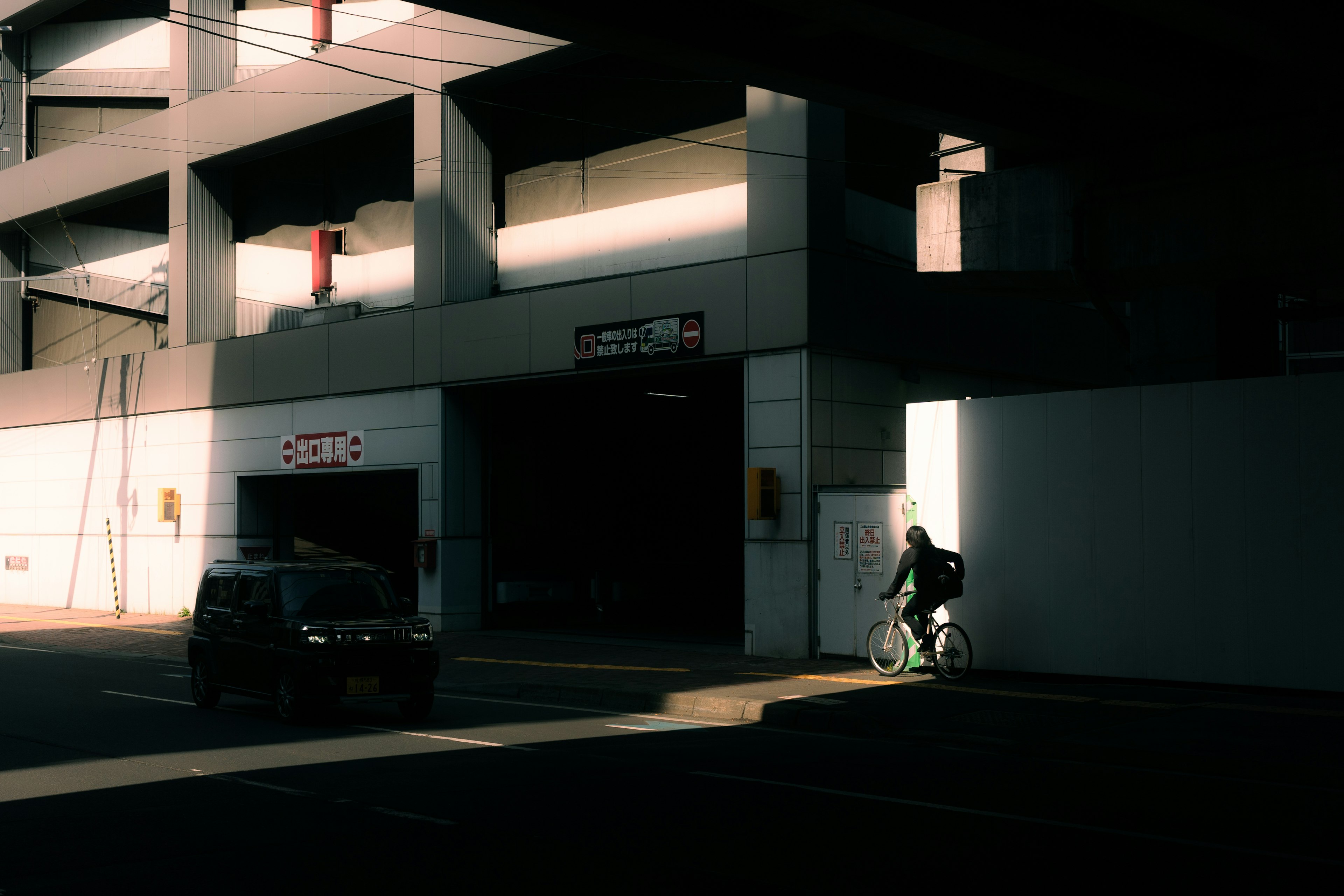 A person riding a bicycle is seen exiting a brightly lit doorway of a parking structure