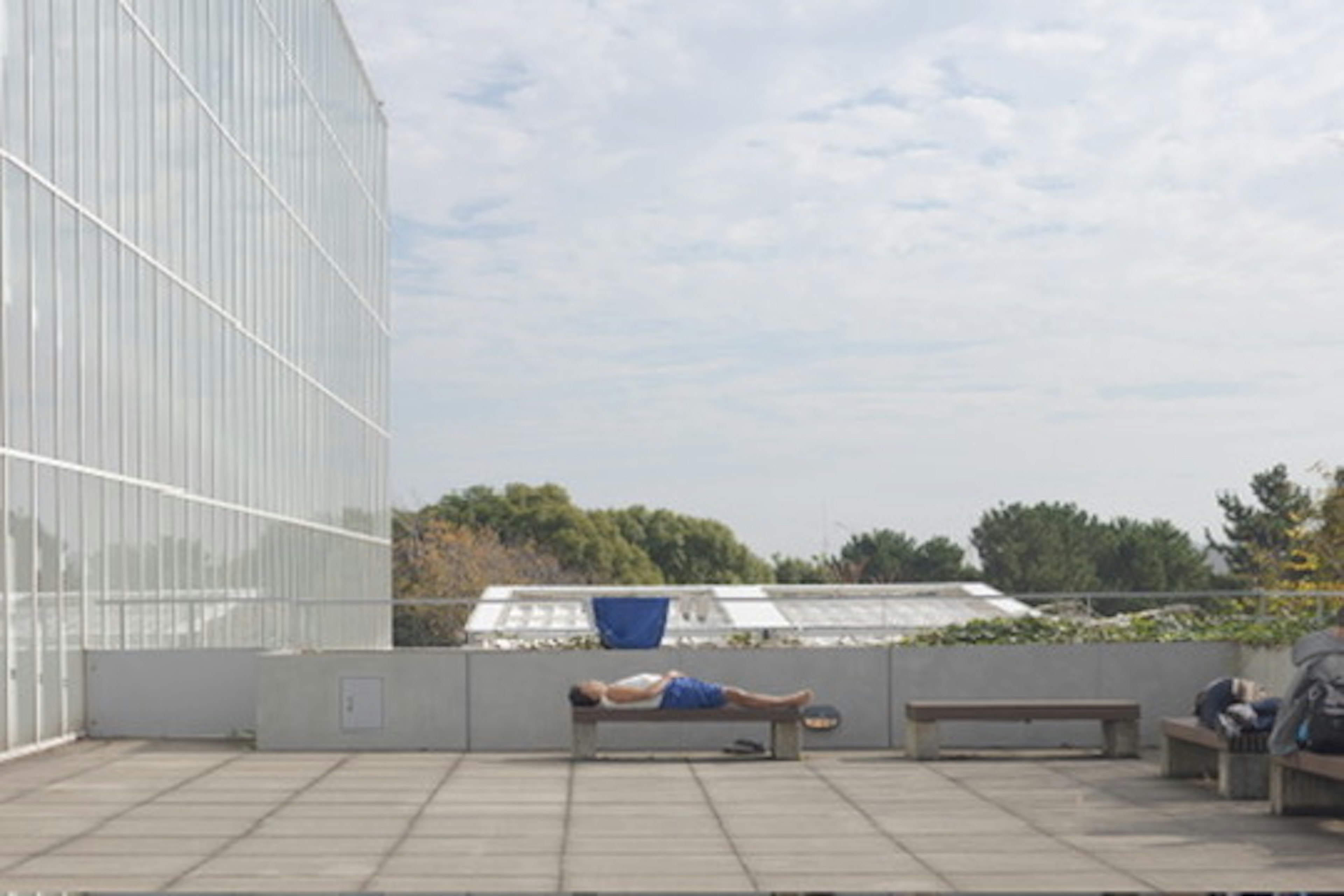 Mann liegt auf einer Außenbank mit blauem Himmel und Wolken in der Nähe eines Glasgebäudes