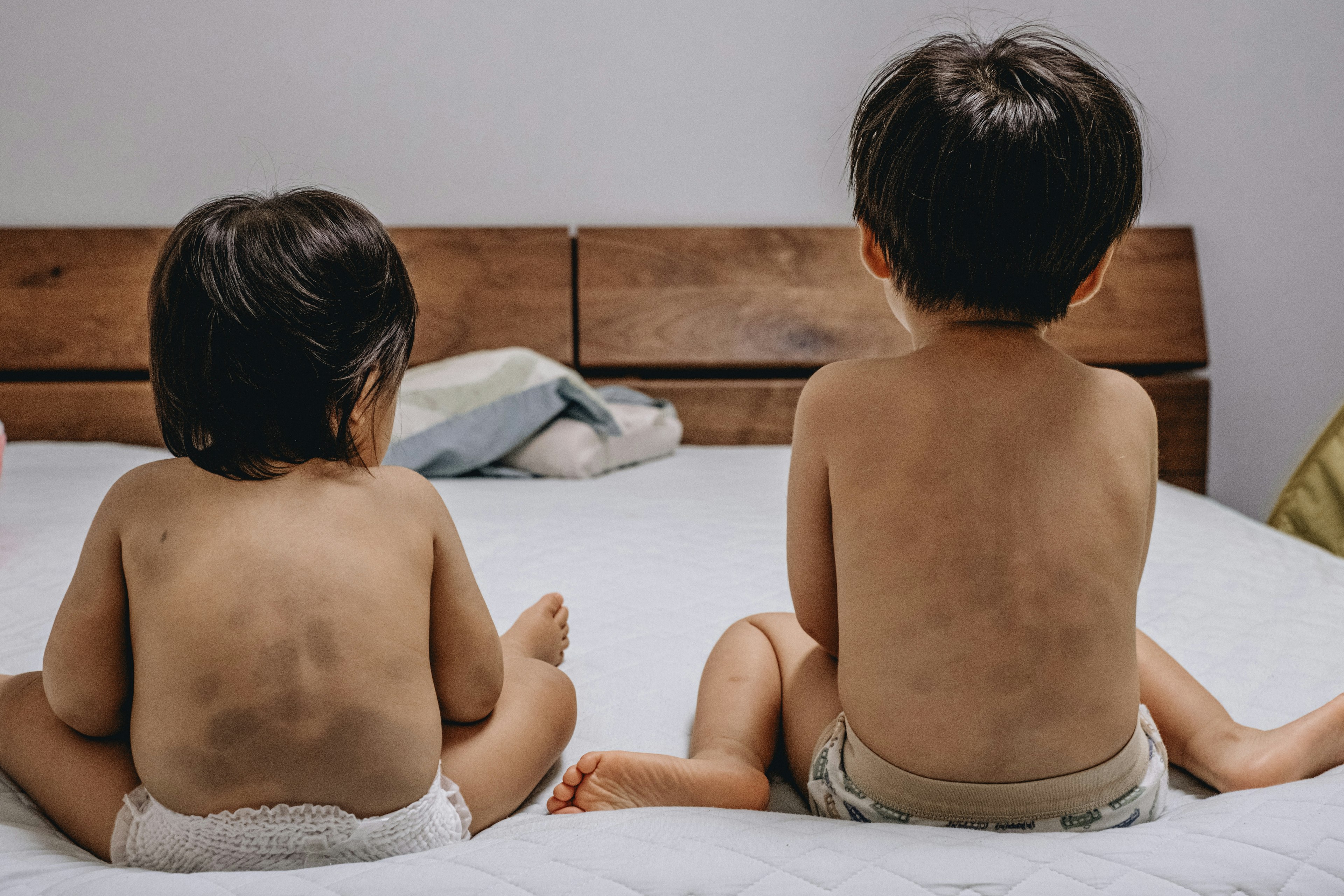 Zwei Kinder sitzen auf einem Bett mit dem Rücken zur Kamera