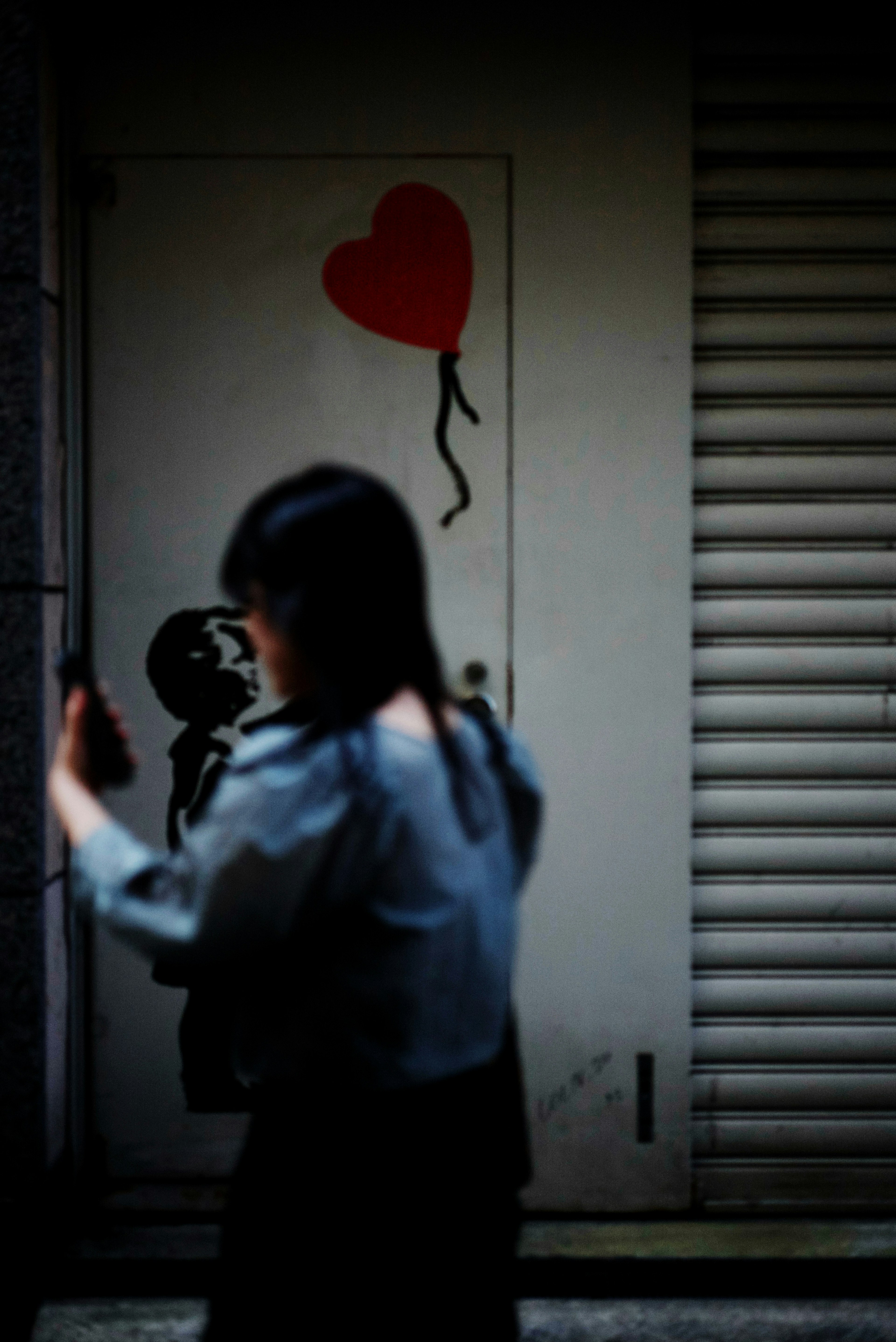 Une femme marchant avec un smartphone devant une porte avec une illustration de ballon en forme de cœur rouge