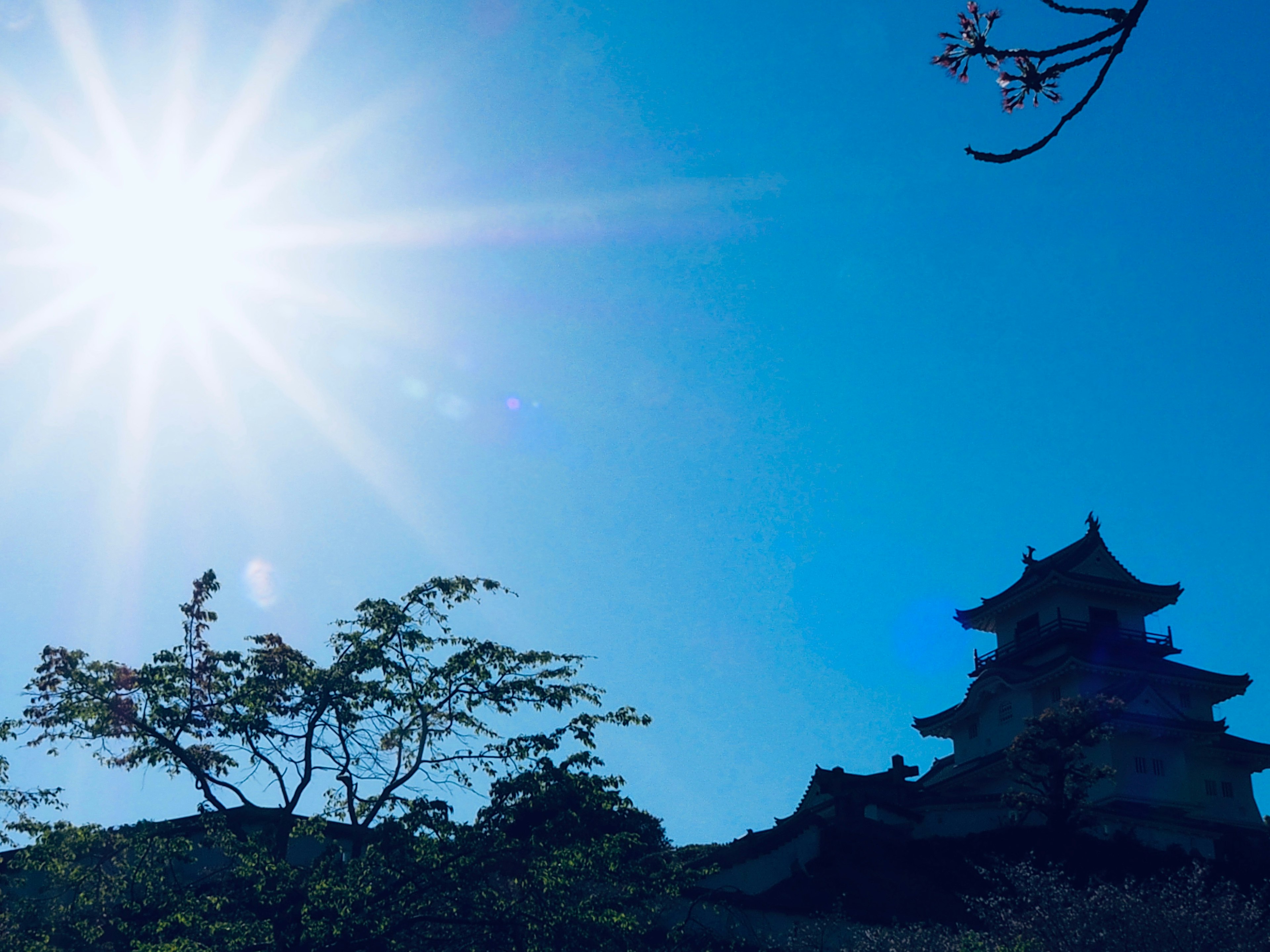 Silhouette eines Schlosses vor einem strahlend blauen Himmel und einer leuchtenden Sonne