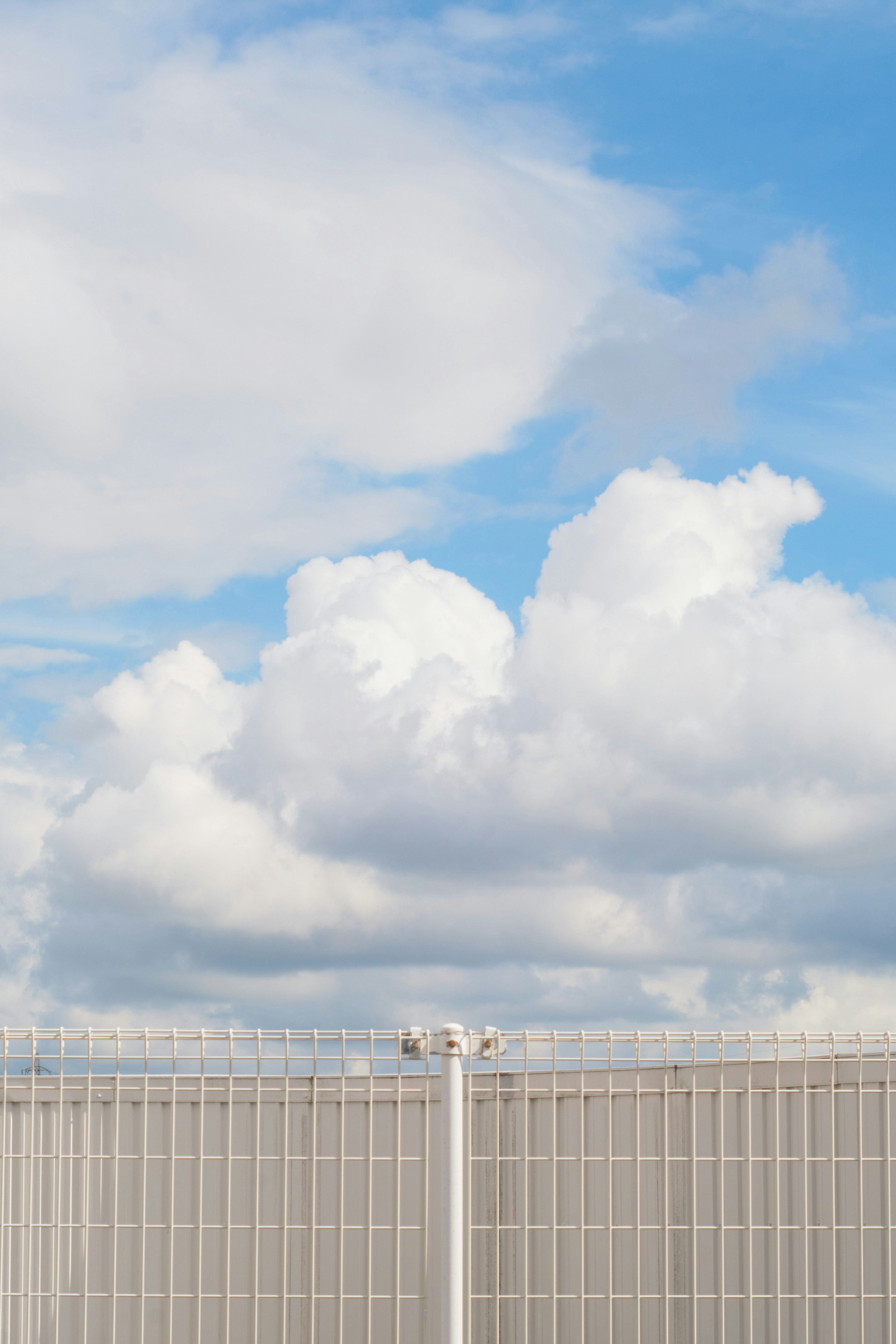 Ein Metallzaun vor einem blauen Himmel mit flauschigen weißen Wolken