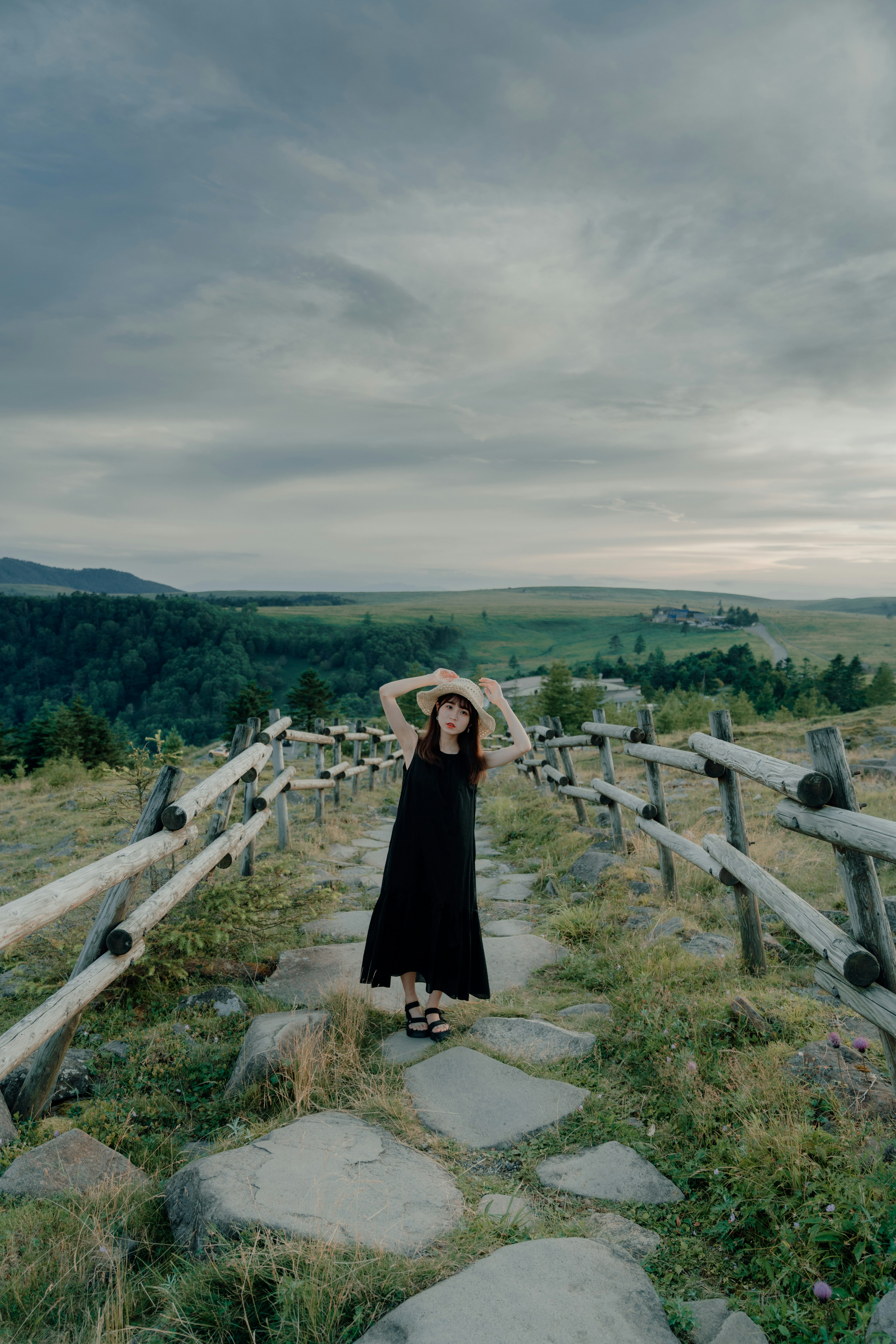 Una mujer con un vestido negro posando en un camino de piedra rodeado de vegetación