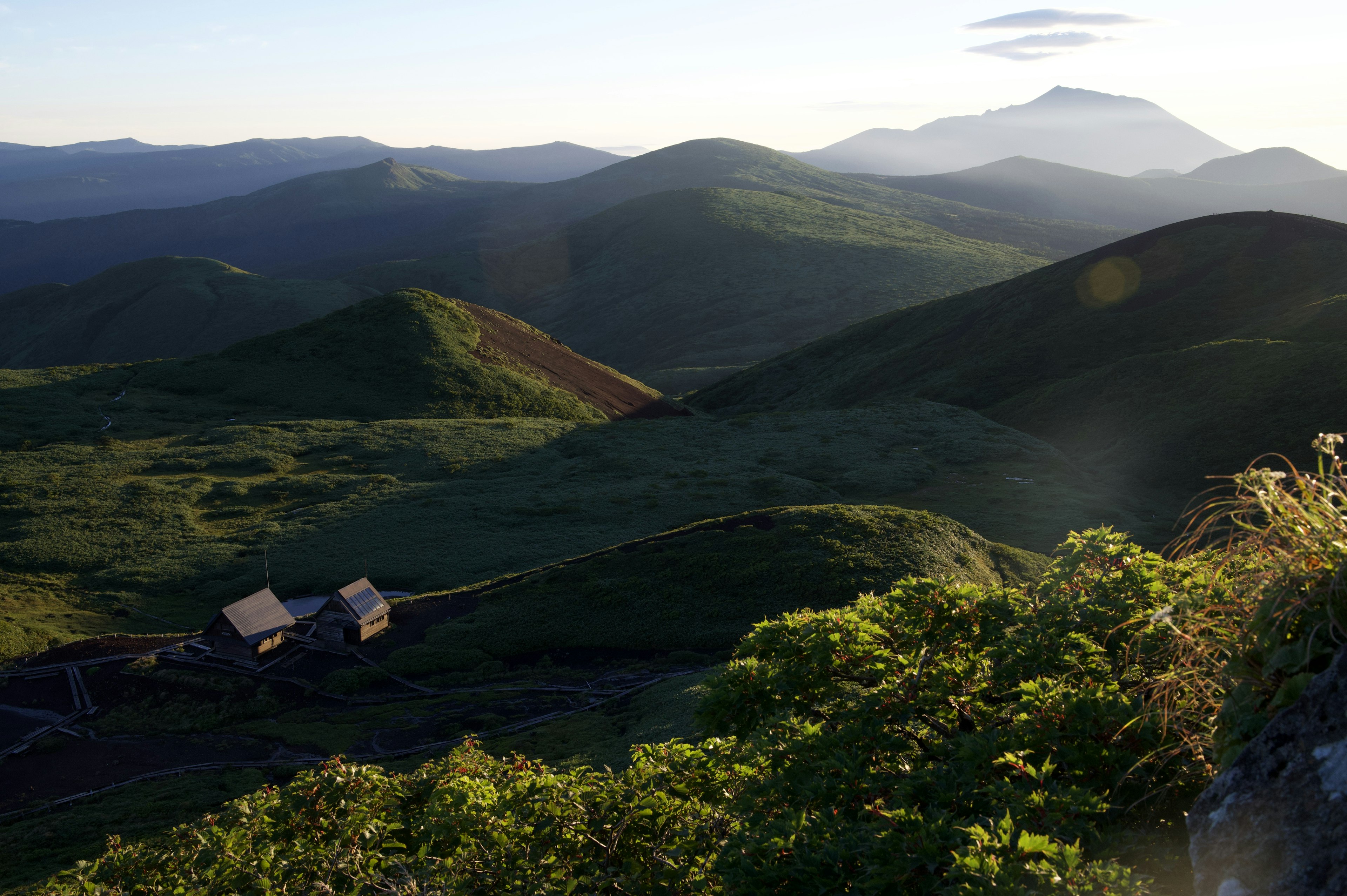 Paisaje escénico con colinas verdes y montañas distantes con una pequeña casa